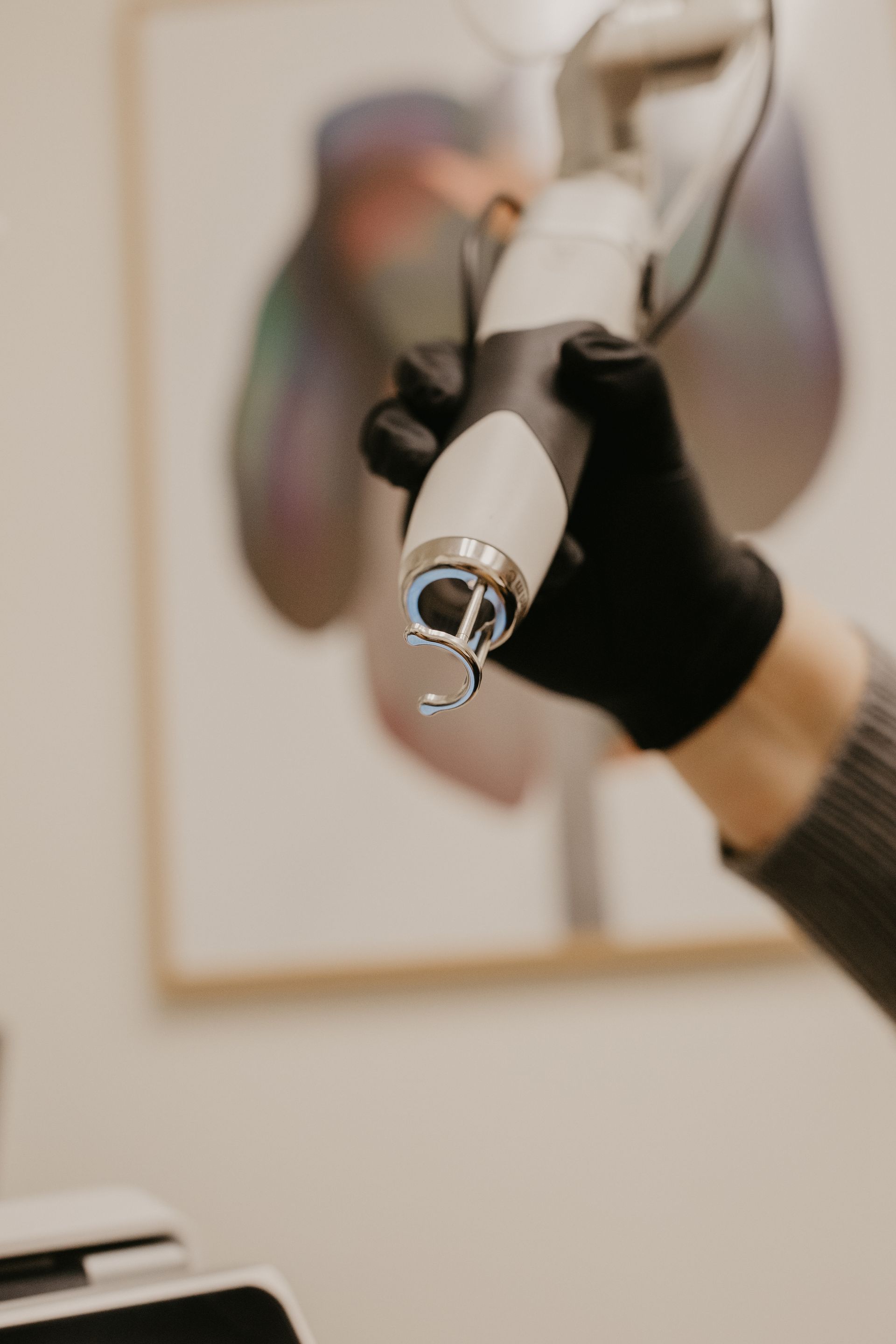 Hand in black glove holding laser device, art in background.