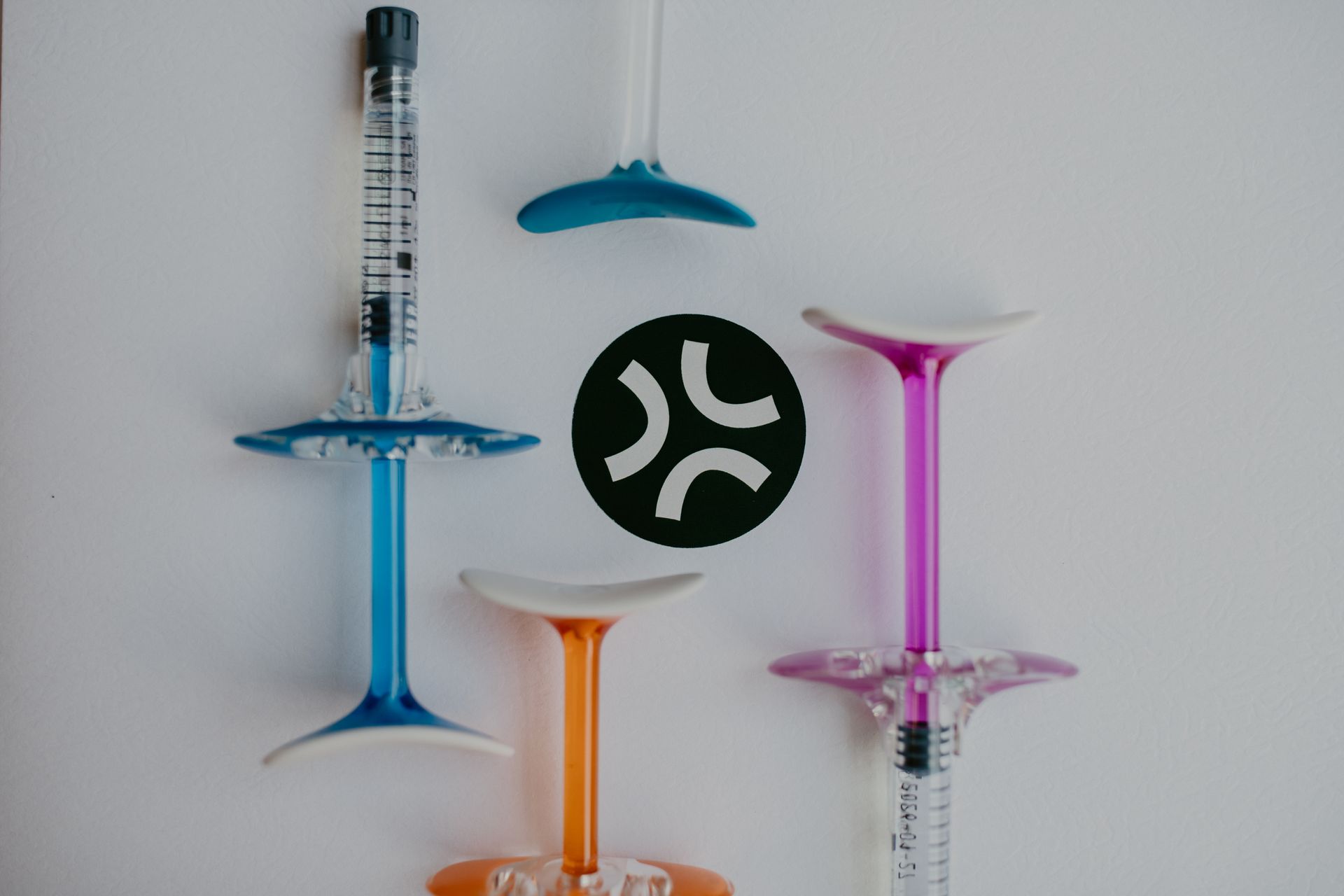 Colorful syringes arranged on a white surface, with a green angry face icon in the center.