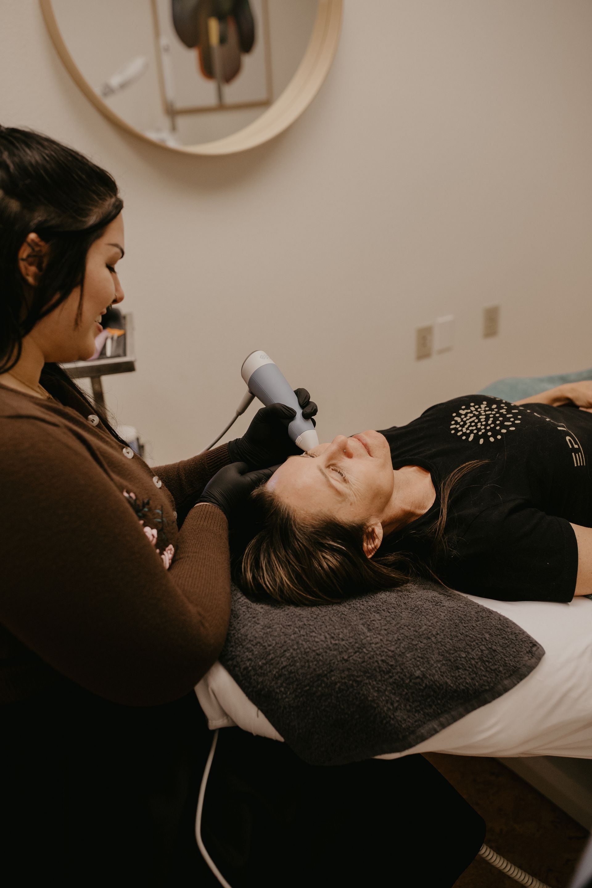 Woman receiving exion rf treatment in a spa. Practitioner uses a device on the client’s face, resting on a towel.
