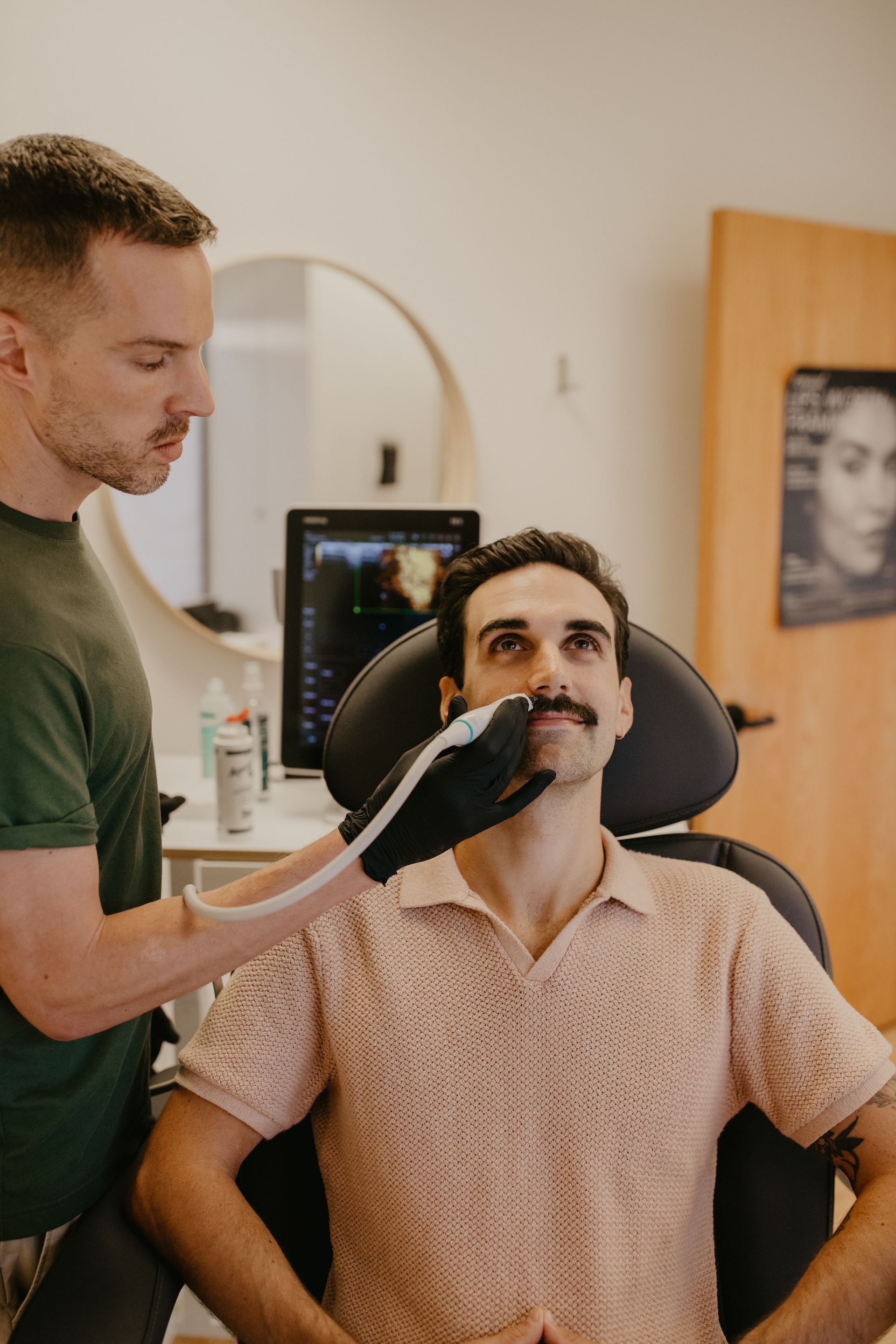 Man getting a facial treatment by an expert. Both men are in a light-filled room.