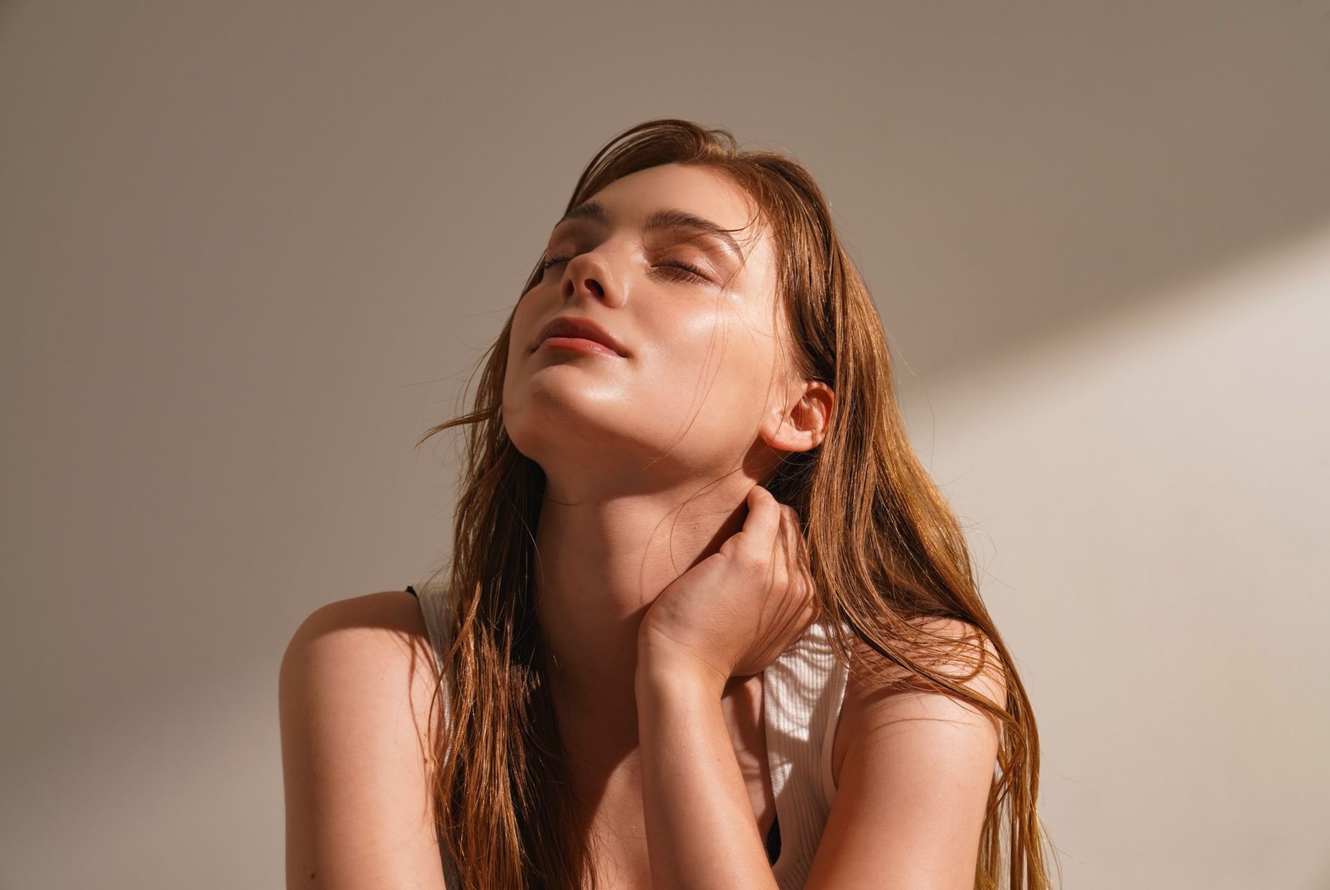 A woman with wet hair is looking up at the sun with her eyes closed.