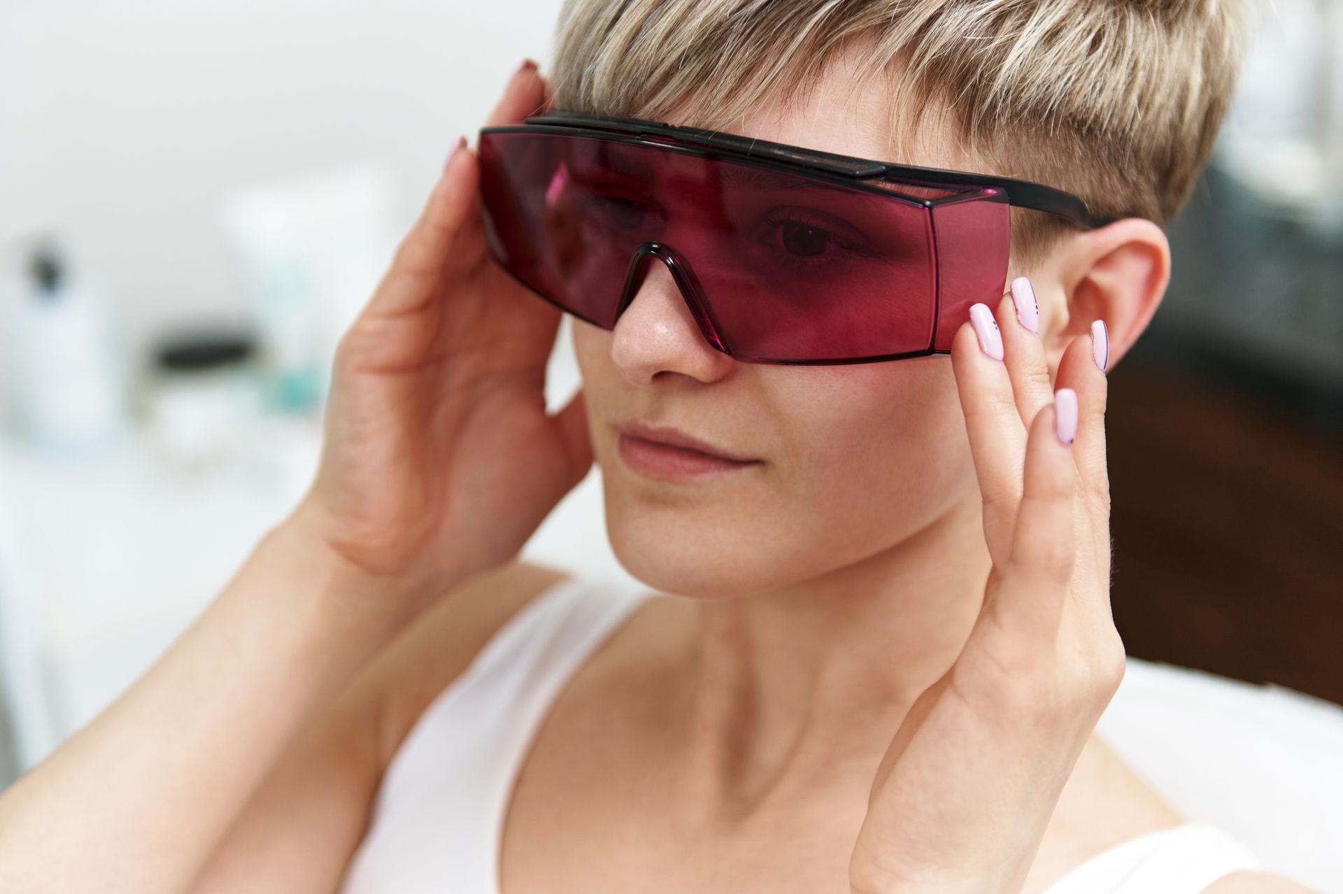 Woman wearing pink-tinted safety glasses, holding them in place with both hands.