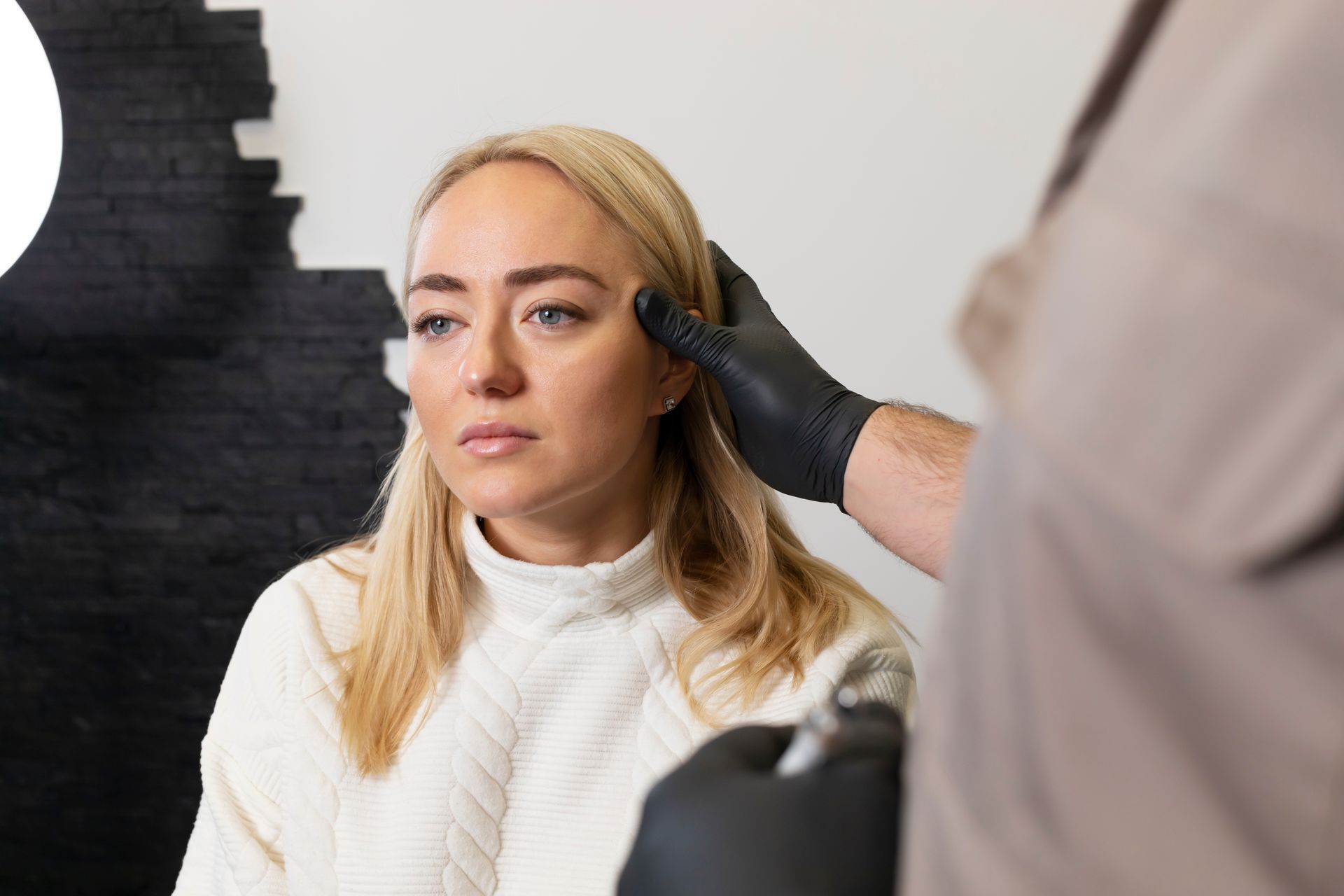A woman is getting her eyebrows done by a man in black gloves.
