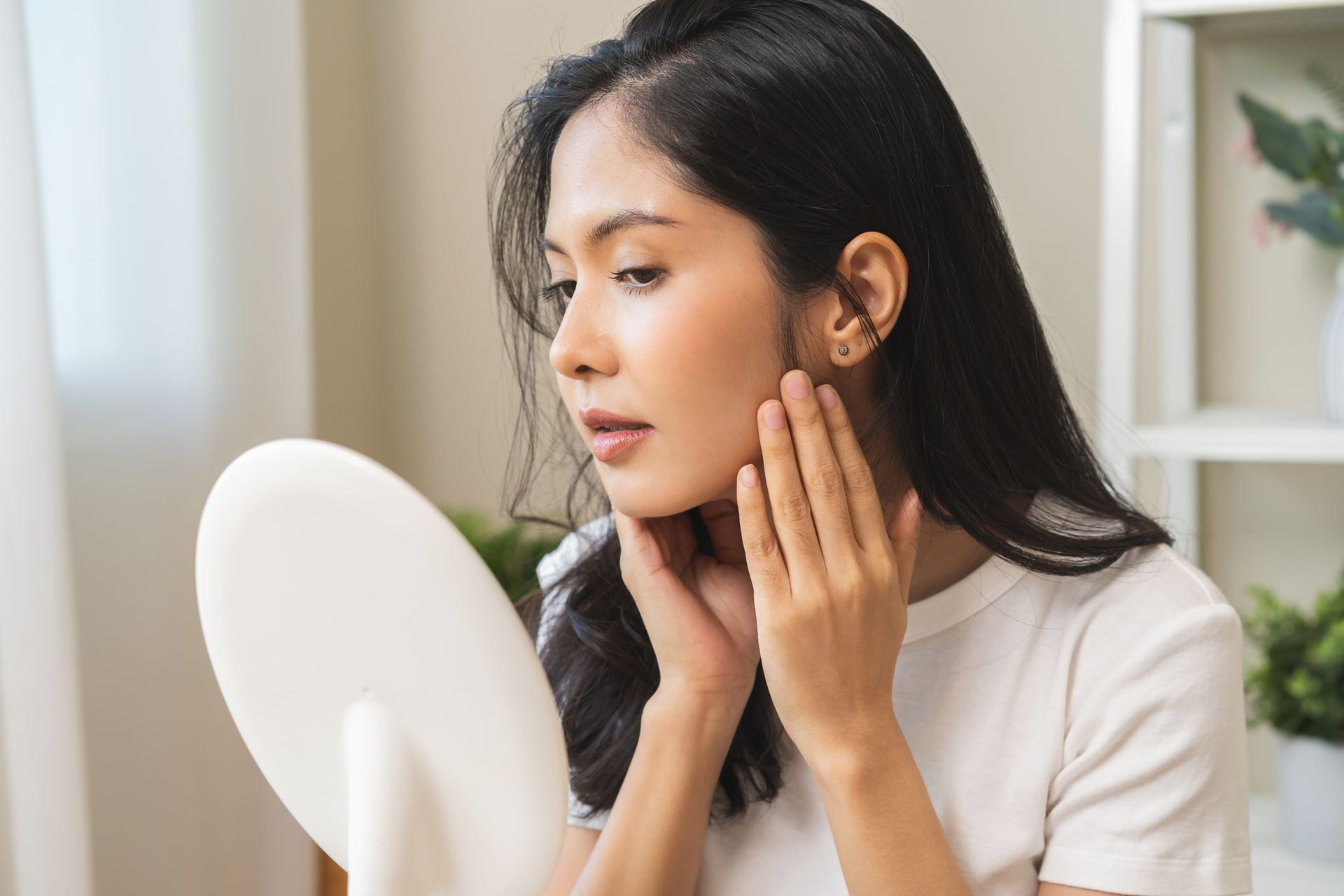 A woman is looking at her face in a mirror.
