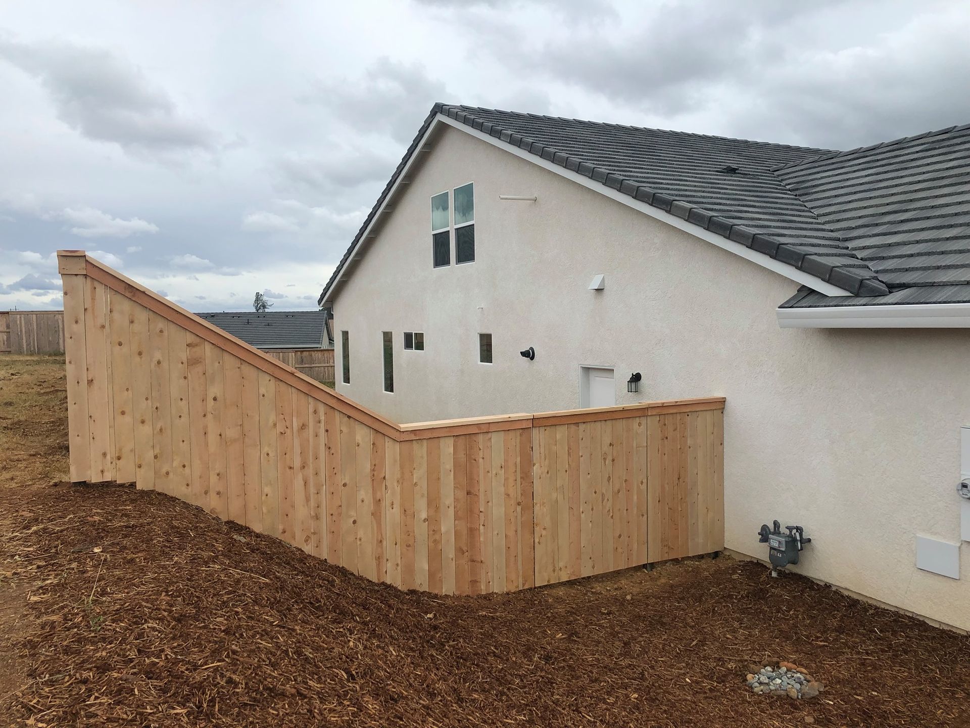 Wooden fence and retaining wall beside a beige house on a cloudy day