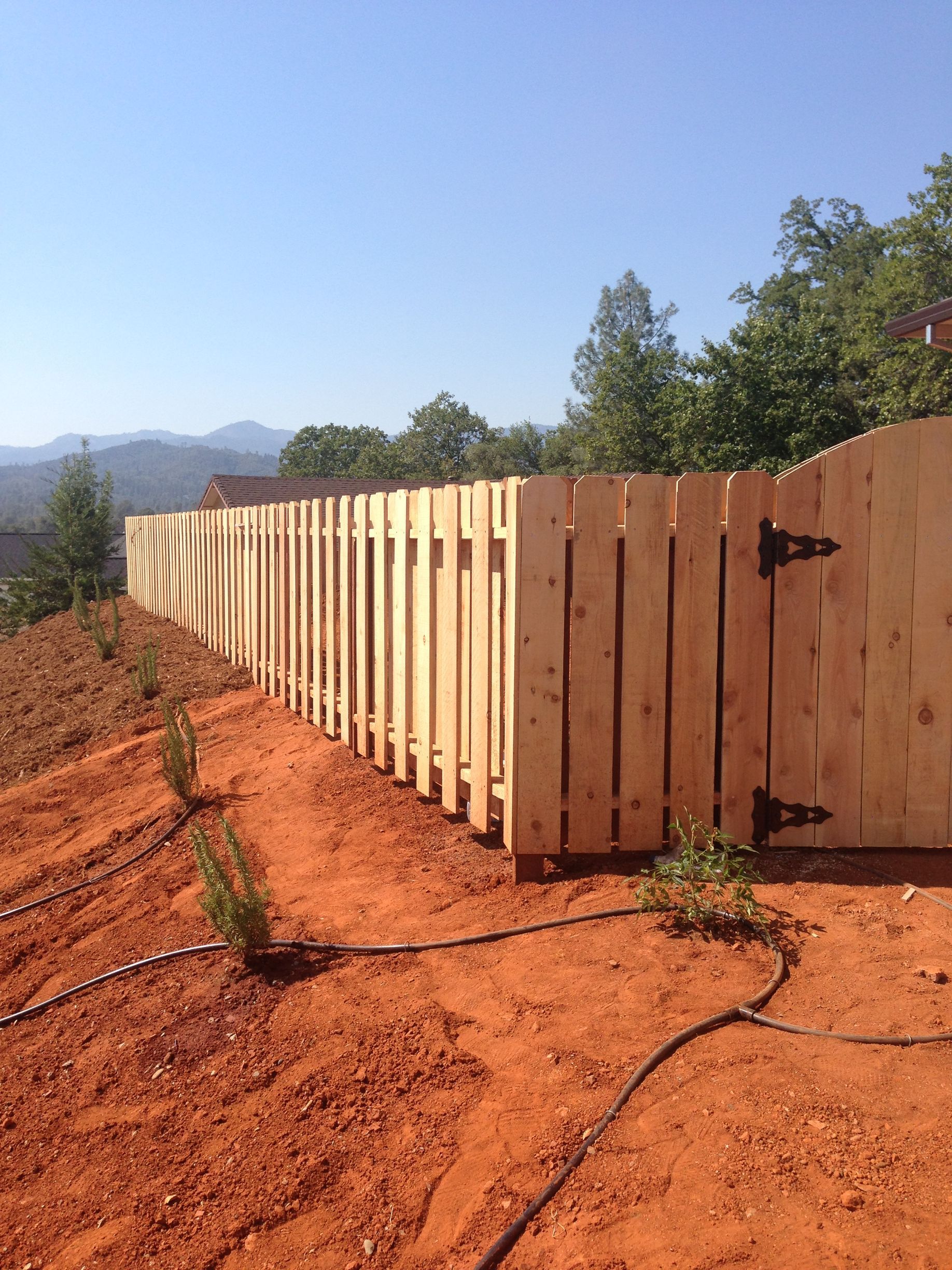 Long wooden fence along a red dirt path under a clear blue sky with mountains in the distance