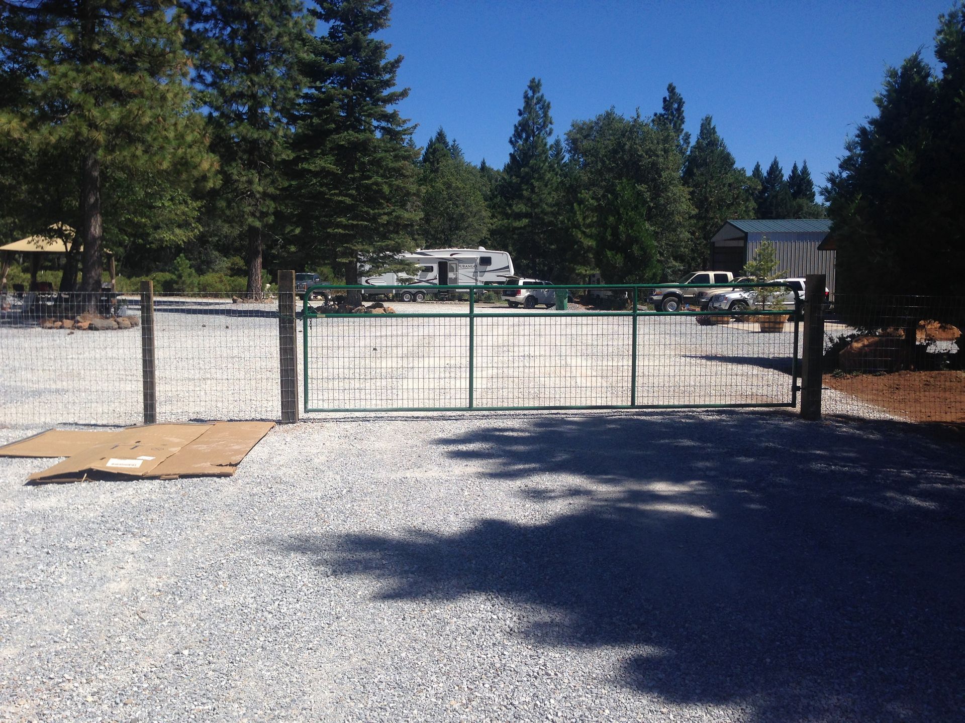 Gated driveway with gravel foreground, trees, and parked RVs under a clear blue sky