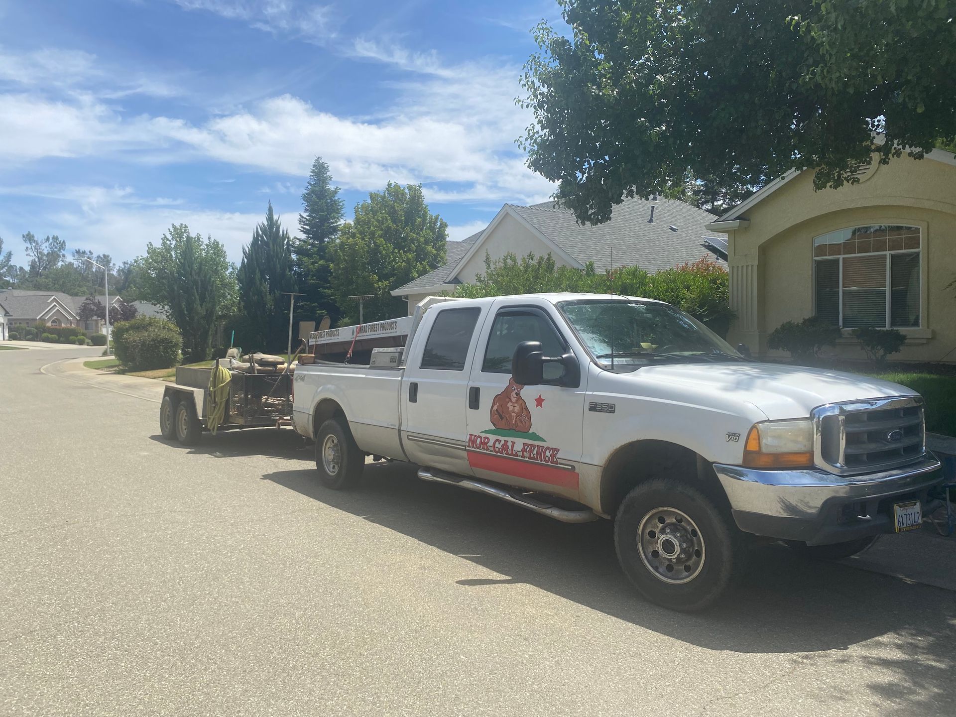White tow truck parked on a sunny suburban street beside a house and trees