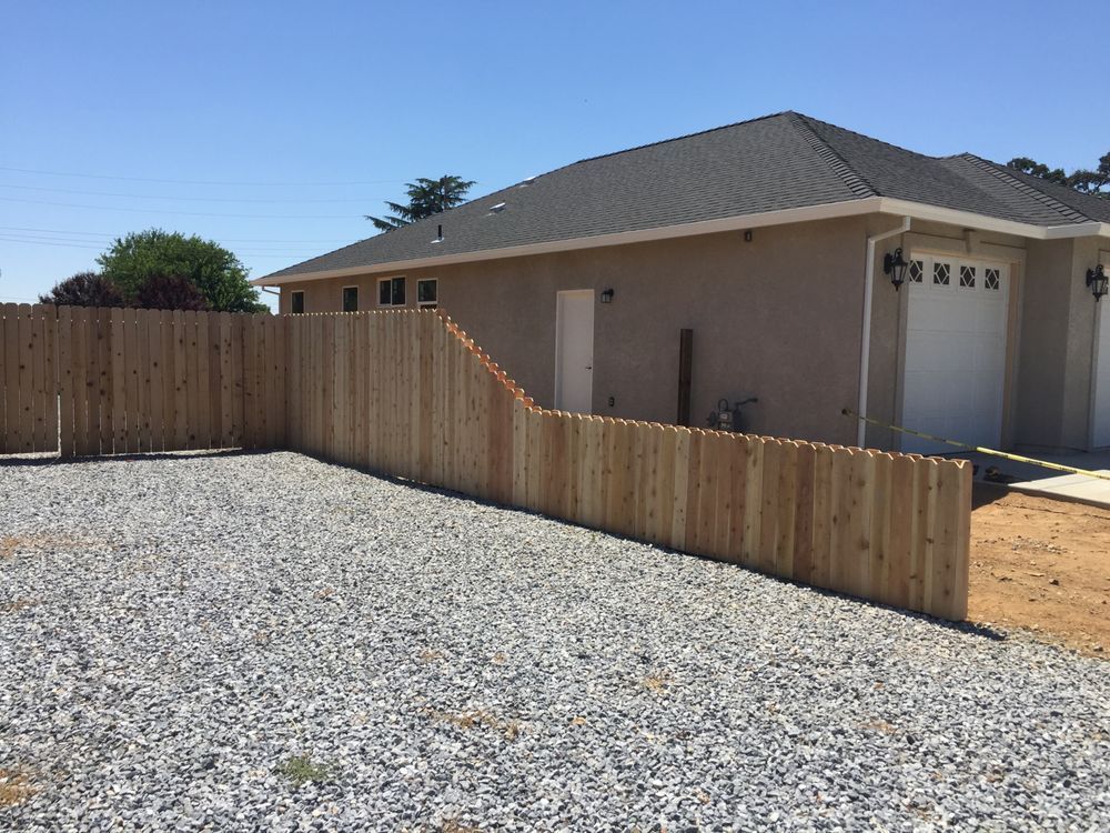 Gravel yard with wooden fence beside a beige house and garage under a clear blue sky
