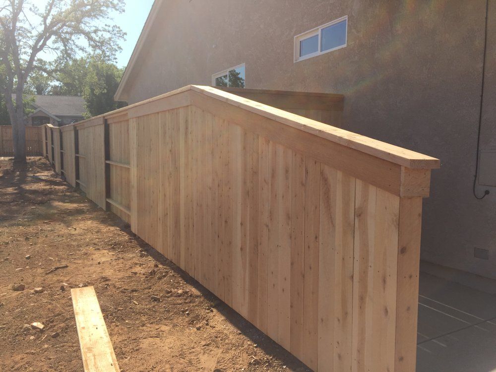 Wooden accessibility ramp and fence beside a house, with a sloped handrail in a backyard.