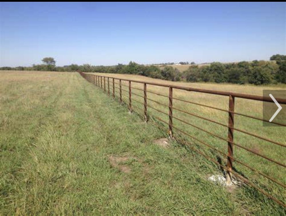 Rusty metal fence along a grassy field under a clear blue sky