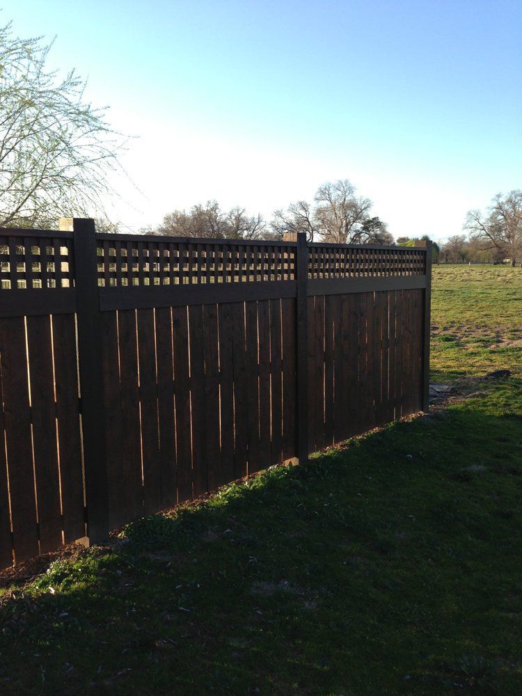 Dark wooden fence beside a grassy field under a clear blue sky