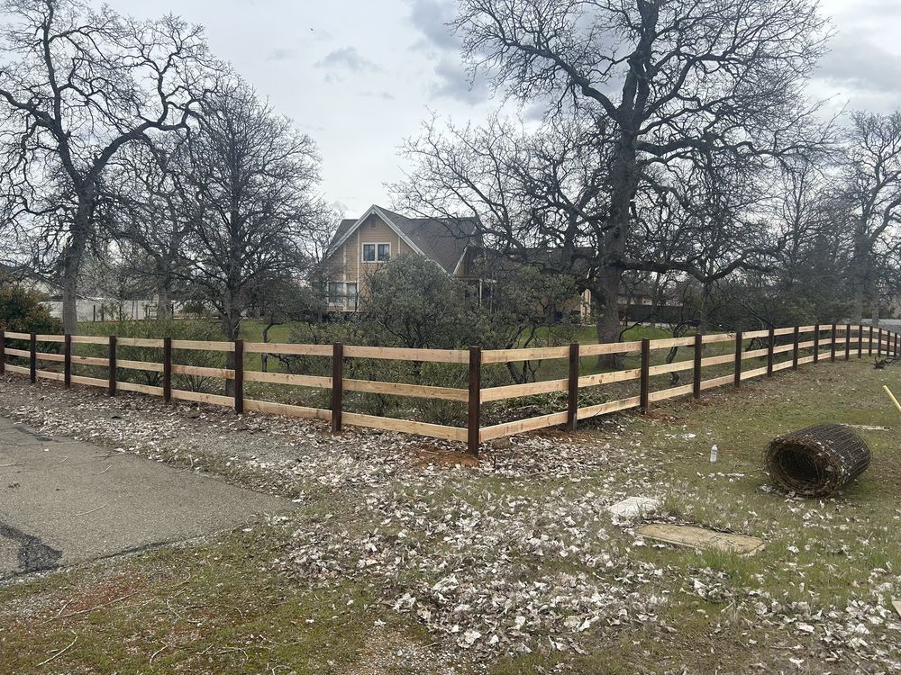Rural house behind a black-and-tan fence, with leafless trees and light snow on the ground.