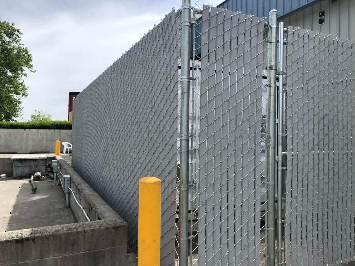 Chain-link fence beside a concrete utility area, with a yellow bollard and cloudy sky.