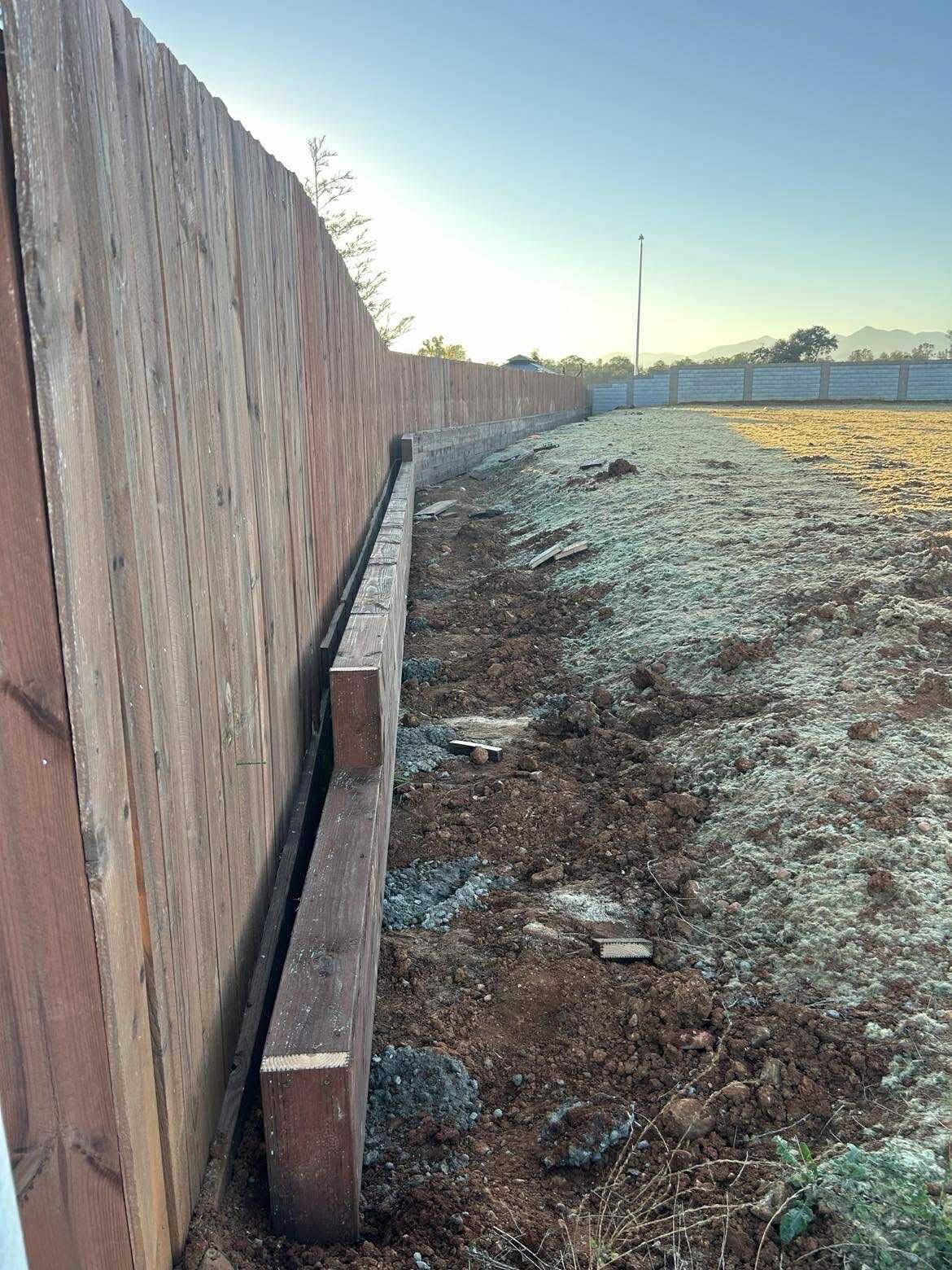 Wooden fence beside a frosty dirt field at sunrise, with a narrow concrete curb along the fence line
