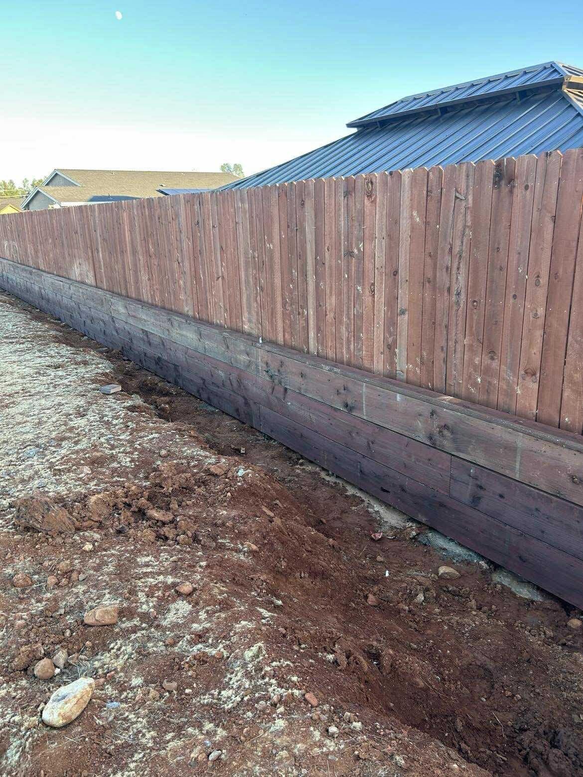 Wooden privacy fence along a dirt lot beside a house with a gray roof