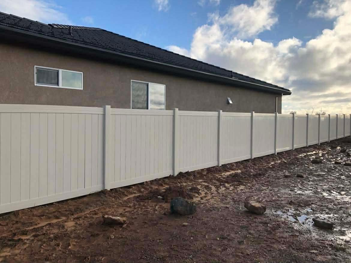 White fence beside a brown house under a cloudy sky, with bare dirt in the foreground