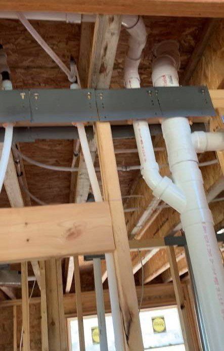 A bunch of pipes are hanging from the ceiling of a house under construction.