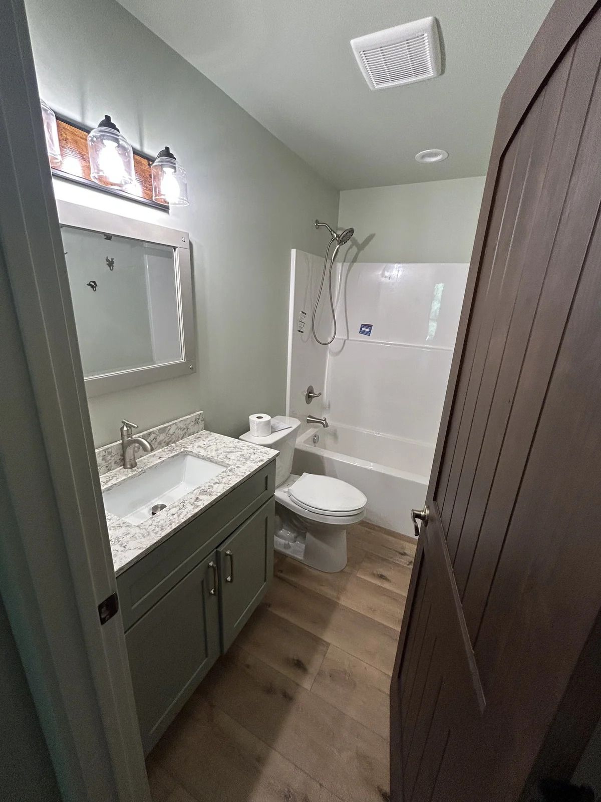 Bathroom with a vanity, toilet, shower/tub combo, and light-colored wood floors.