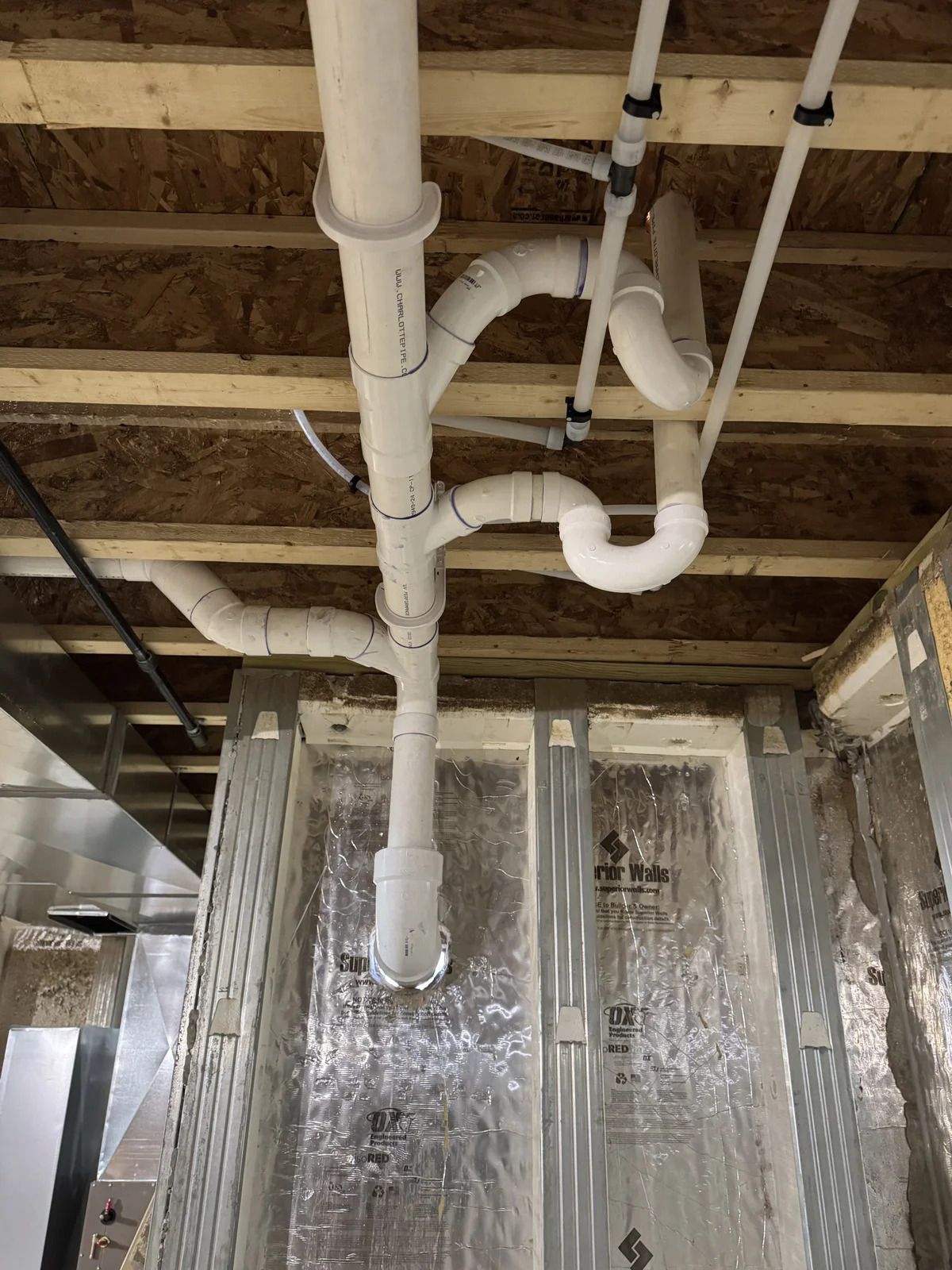 Plumbing pipes, mostly white PVC, installed in a basement ceiling; insulation visible.