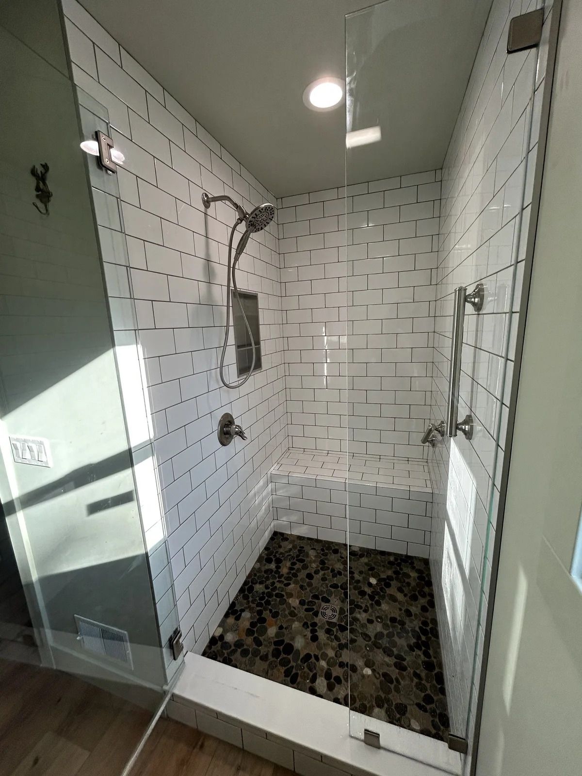 Shower with white subway tile walls, pebble floor, glass doors, and a built-in seat.