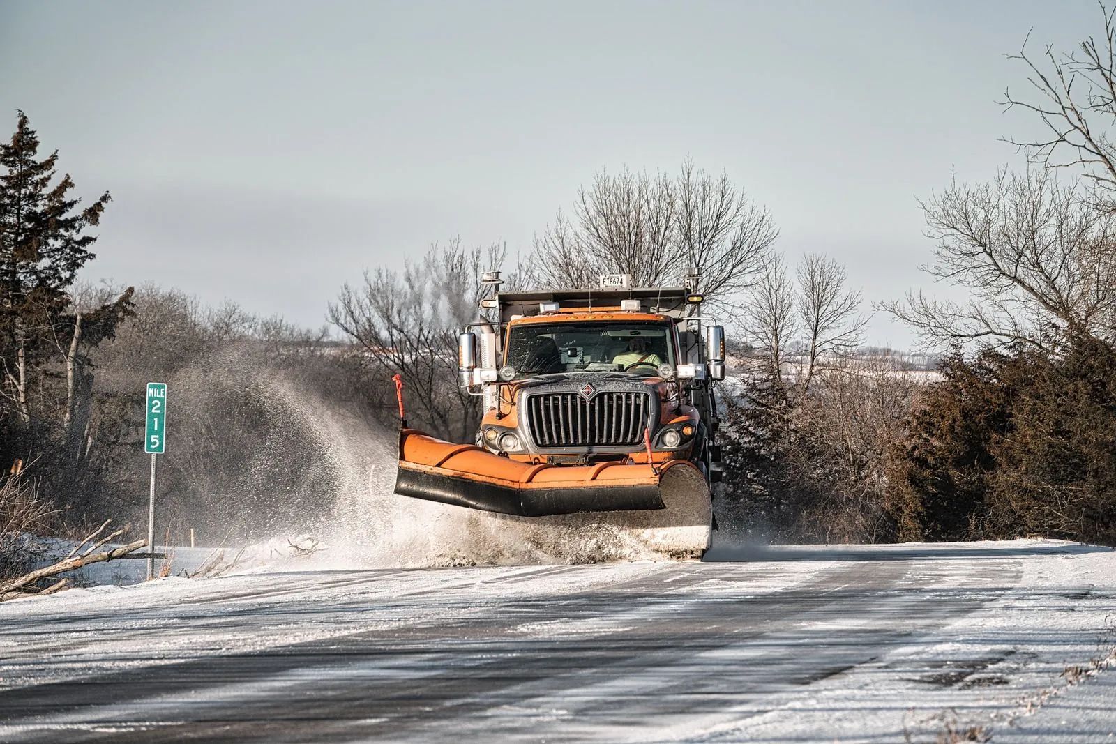 Snowplow plowing a snow-covered road, spraying slush.