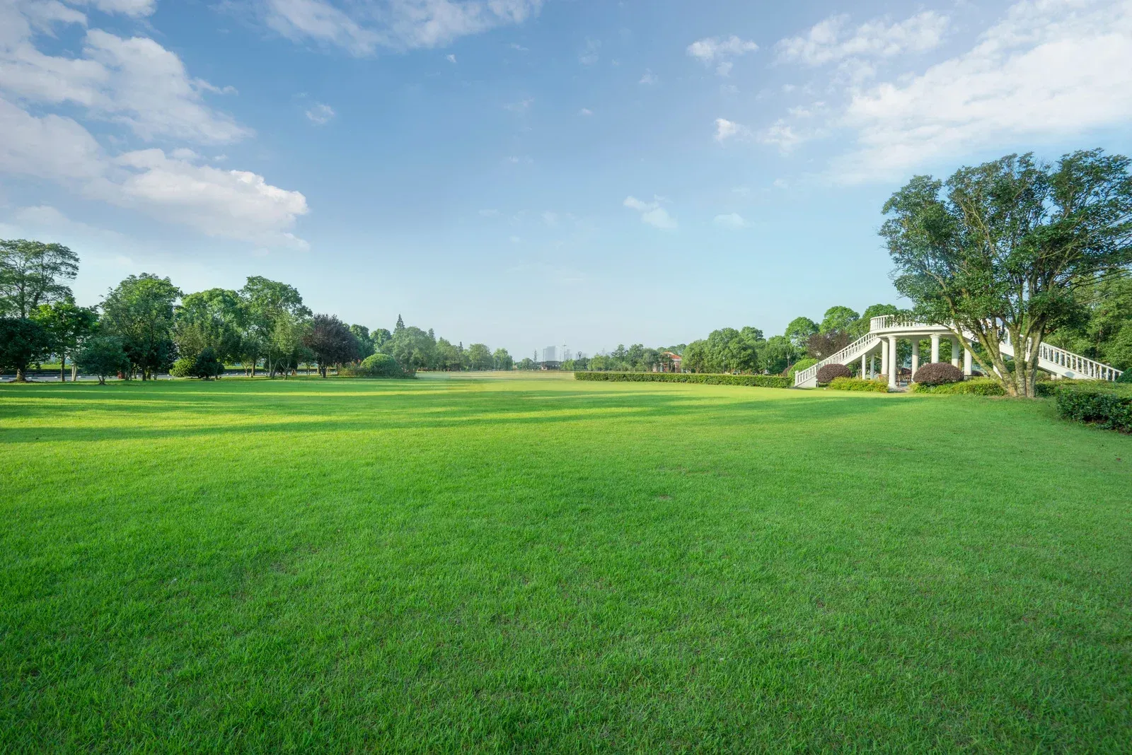 Vast green lawn under a blue sky, trees on the edges, and a white architectural structure on the right.