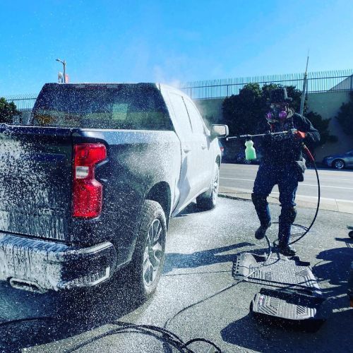 A man is washing a truck with a high pressure washer.