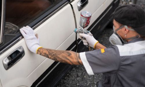 A man with a tattoo on his arm is spray painting a white car.