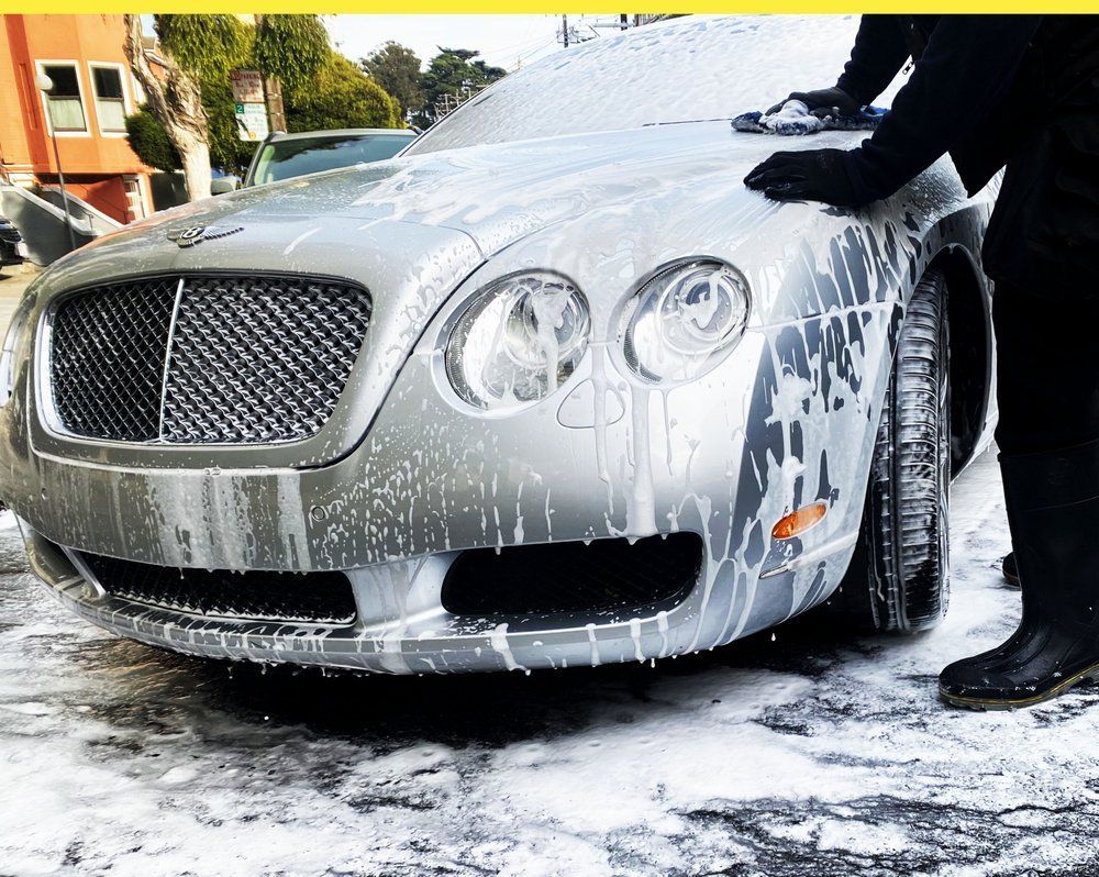 A person is washing a bentley car with soap and water.