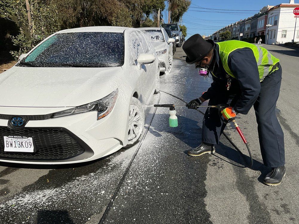 A man is washing a white car on the side of the road.