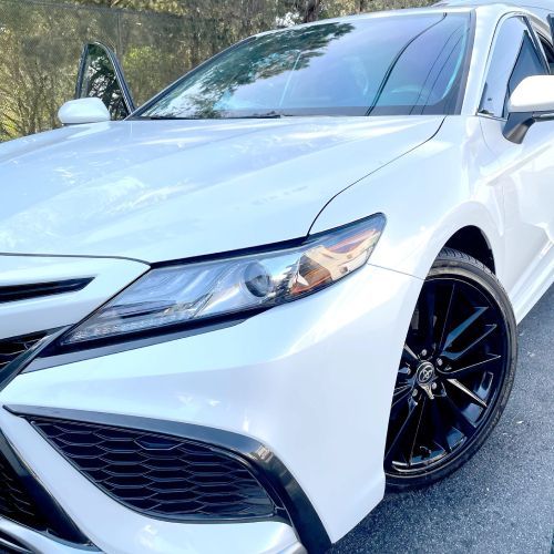 A white car with black wheels is parked on the side of the road.