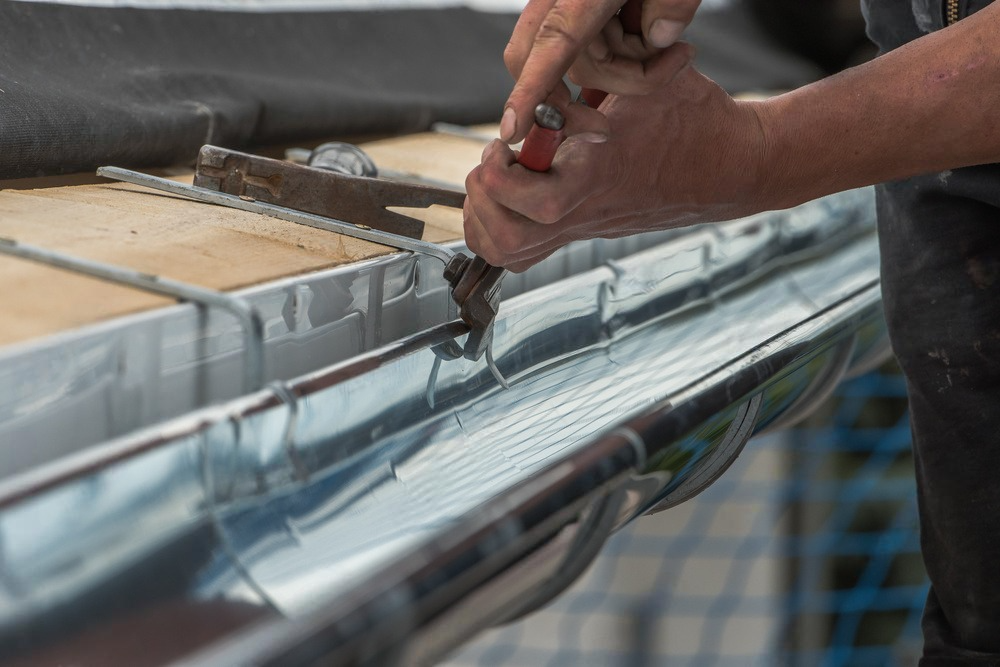 a person is cutting a metal gutter with a pair of scissors .