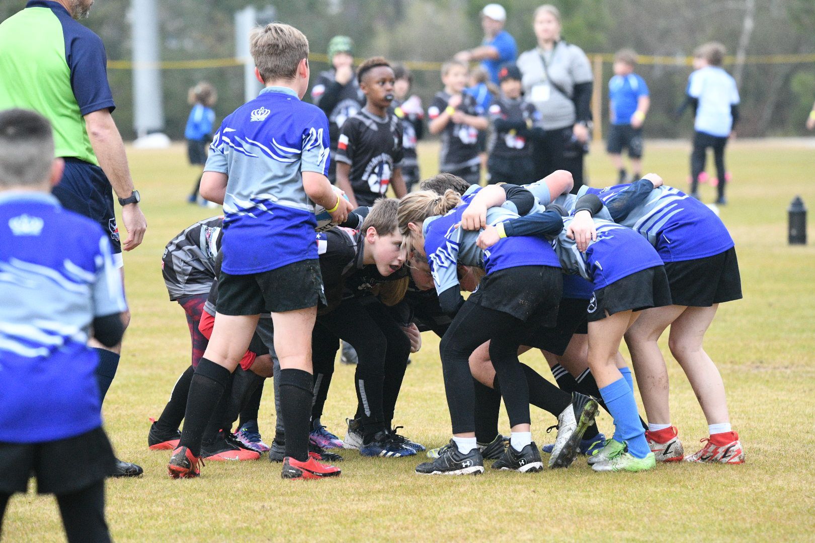 Youth rugby players huddle together on a grassy field in blue and black uniforms.