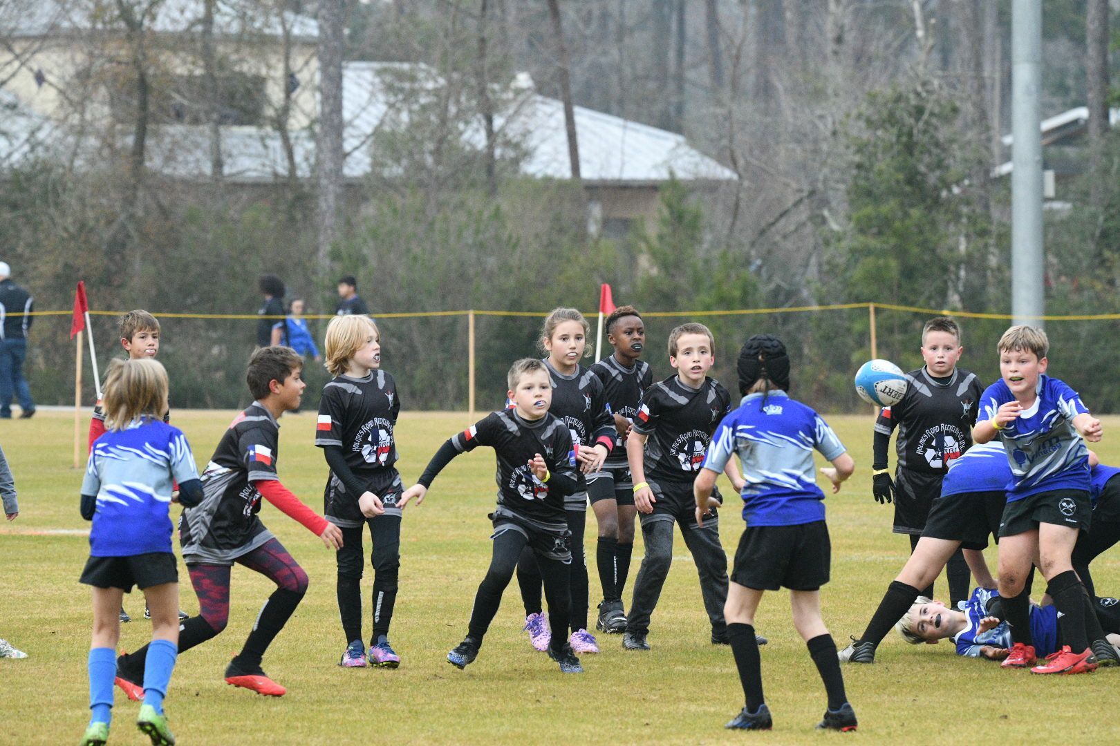 Youth rugby players in black and blue uniforms on a green field.