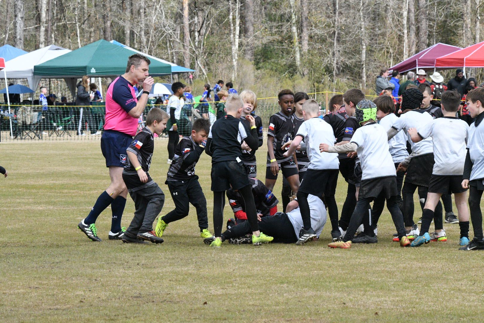 Rugby match: players clustered around a player on the ground, referee observing.