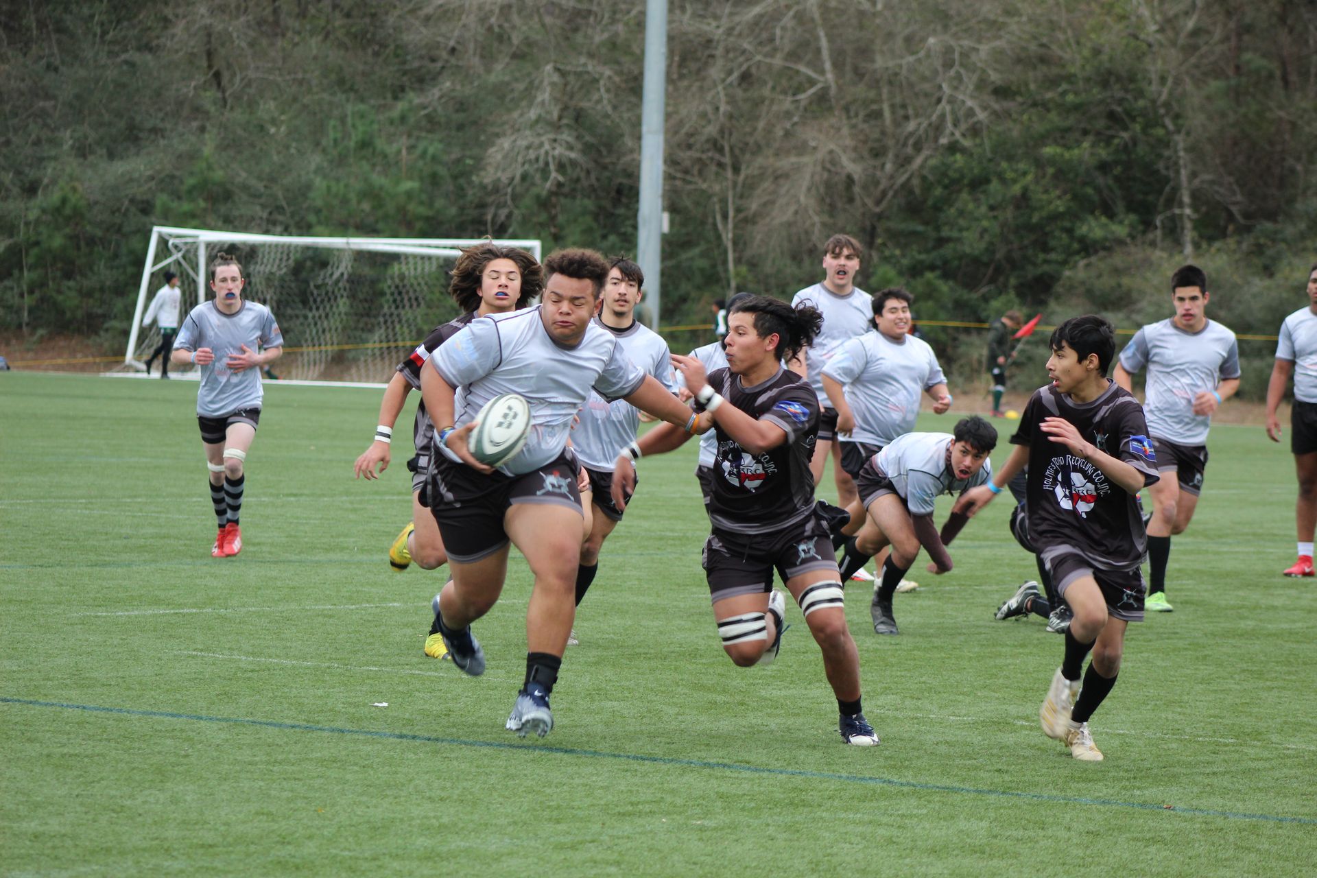 Rugby players on a green field, one with the ball being pursued by others.