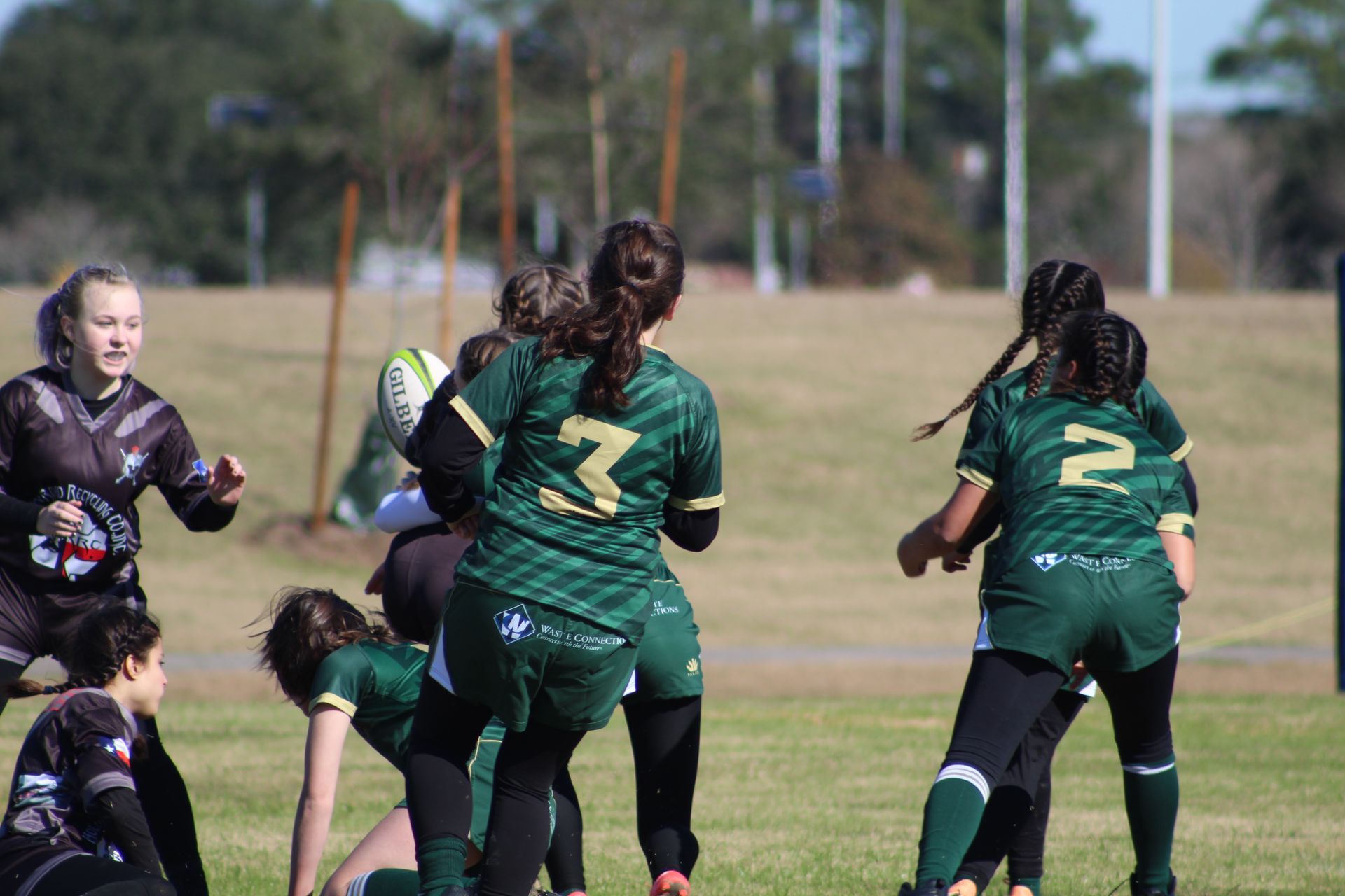 Rugby players in green and black uniforms on a field, some running and focused on the ball.