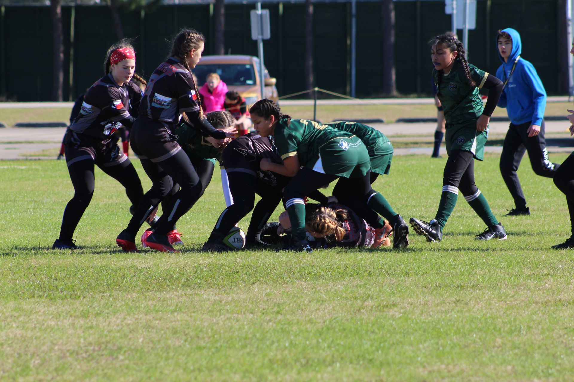 Rugby players in green and black uniforms in a scrum on a green field.