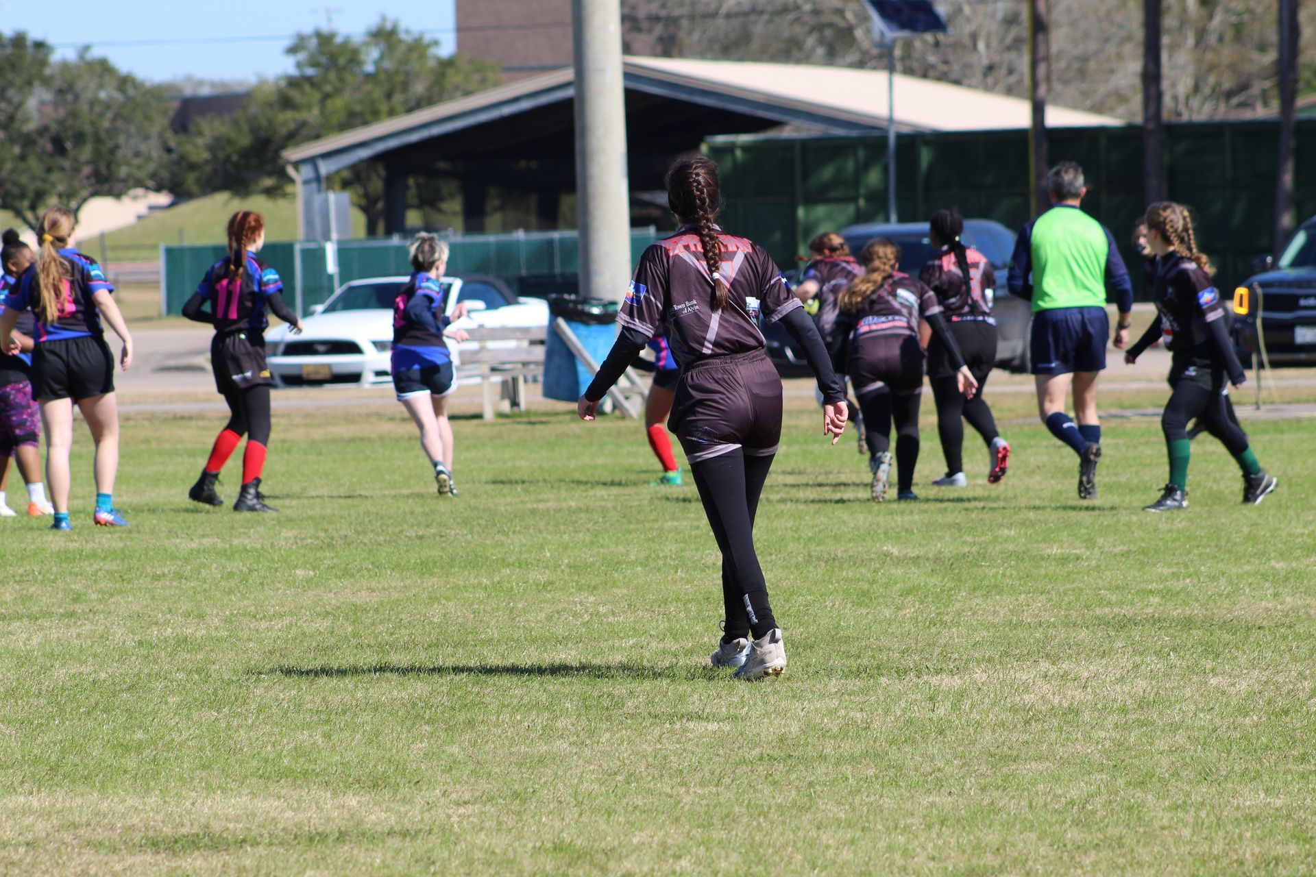 playing rugby on a green field under a sunny sky. Several players in black and purple uniforms are running and interacting.