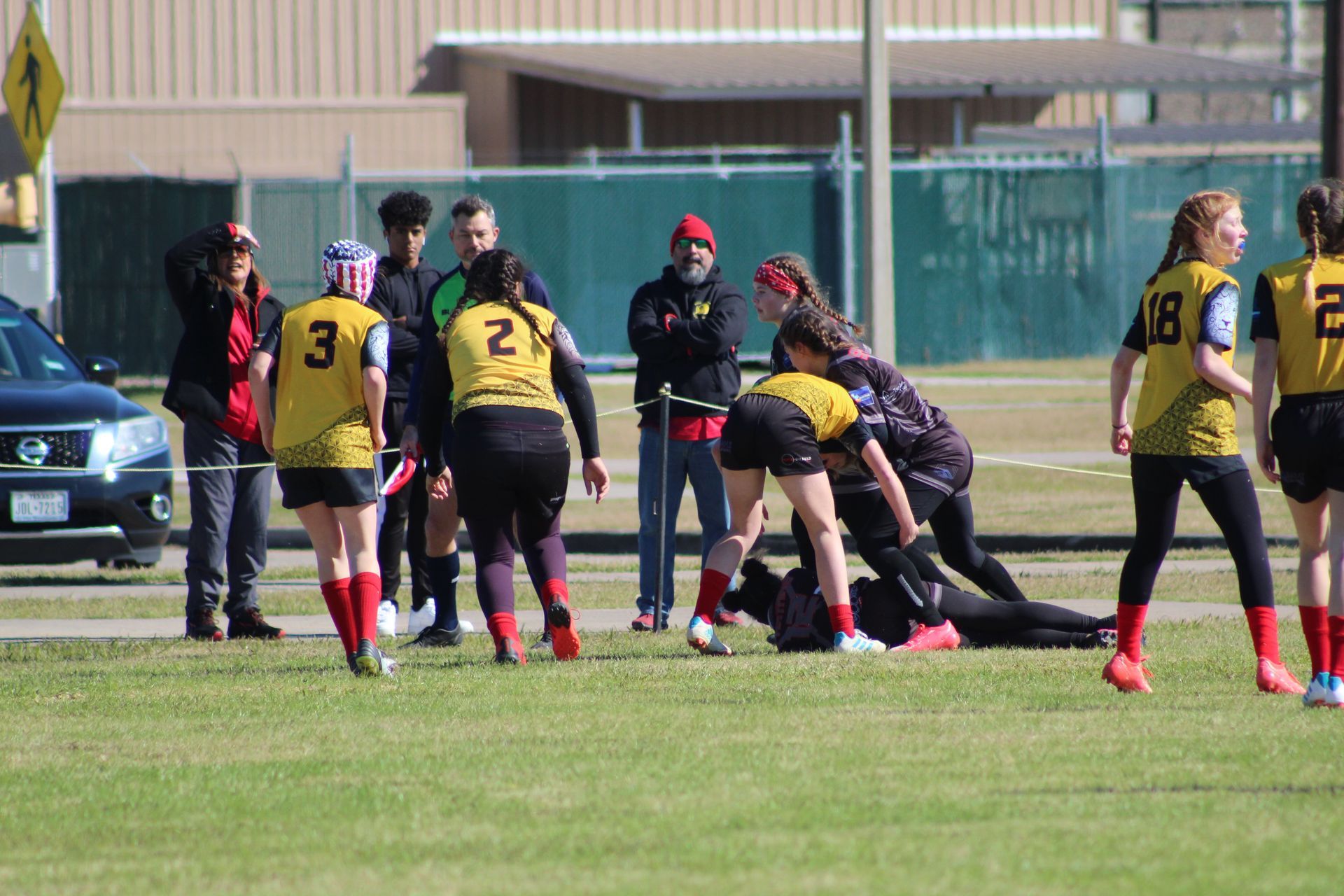 Rugby players in yellow jerseys, black shorts, and red socks on a green field. Players on the ground, others watching.