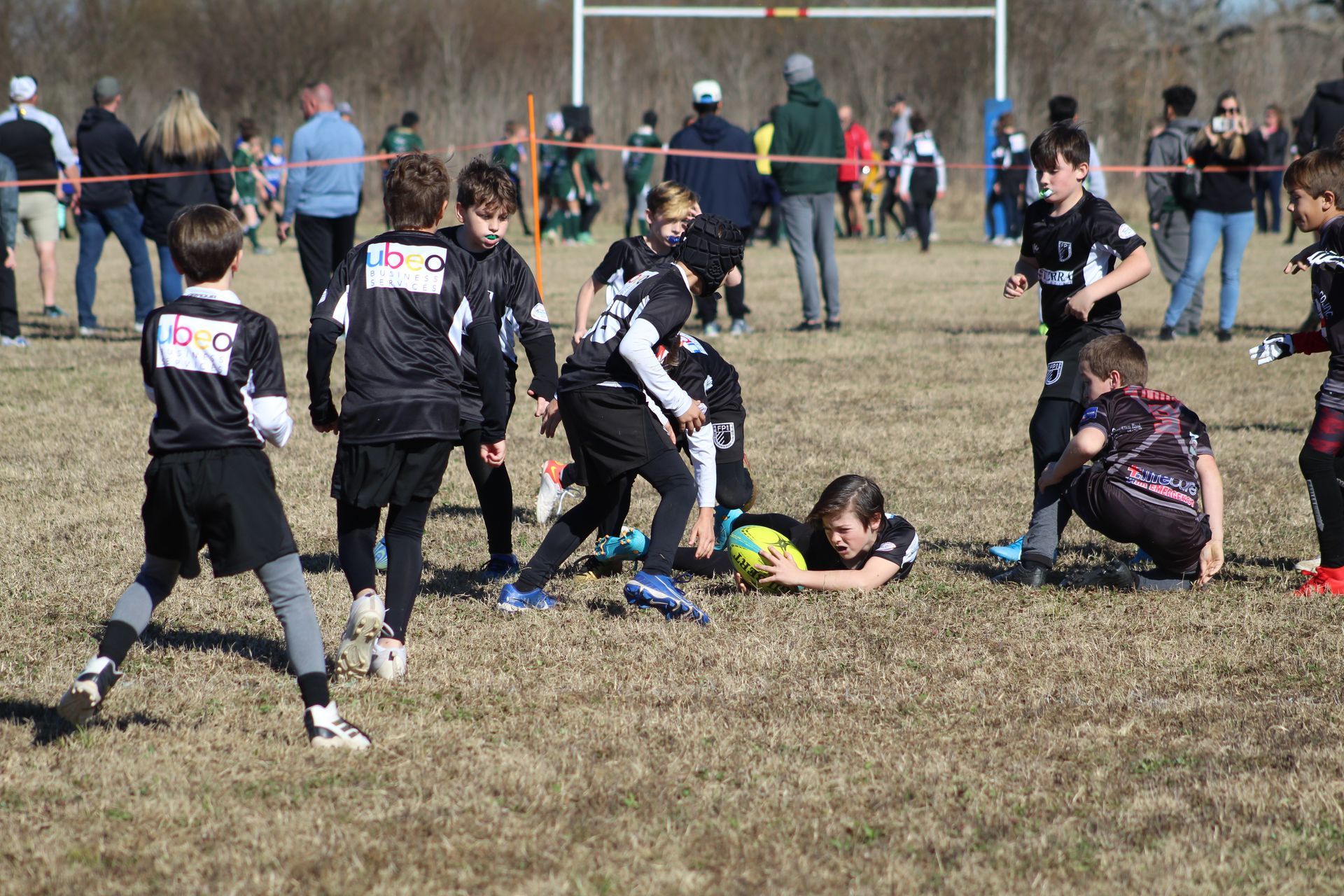 Children playing rugby on a field. One player dives to ground, reaching for the ball; others surround.