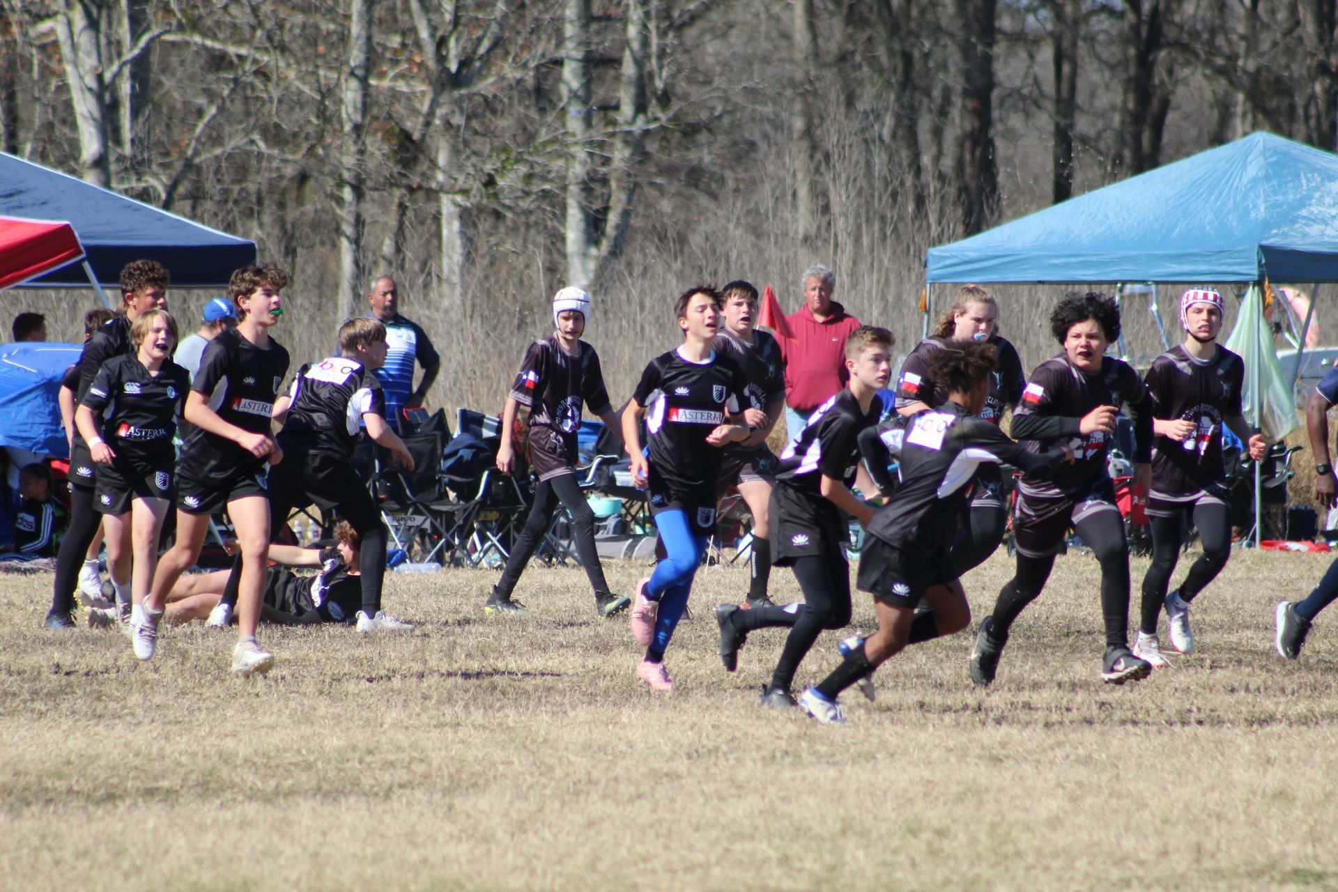 A group of athletes in black jerseys running on a grass field under a blue tent.