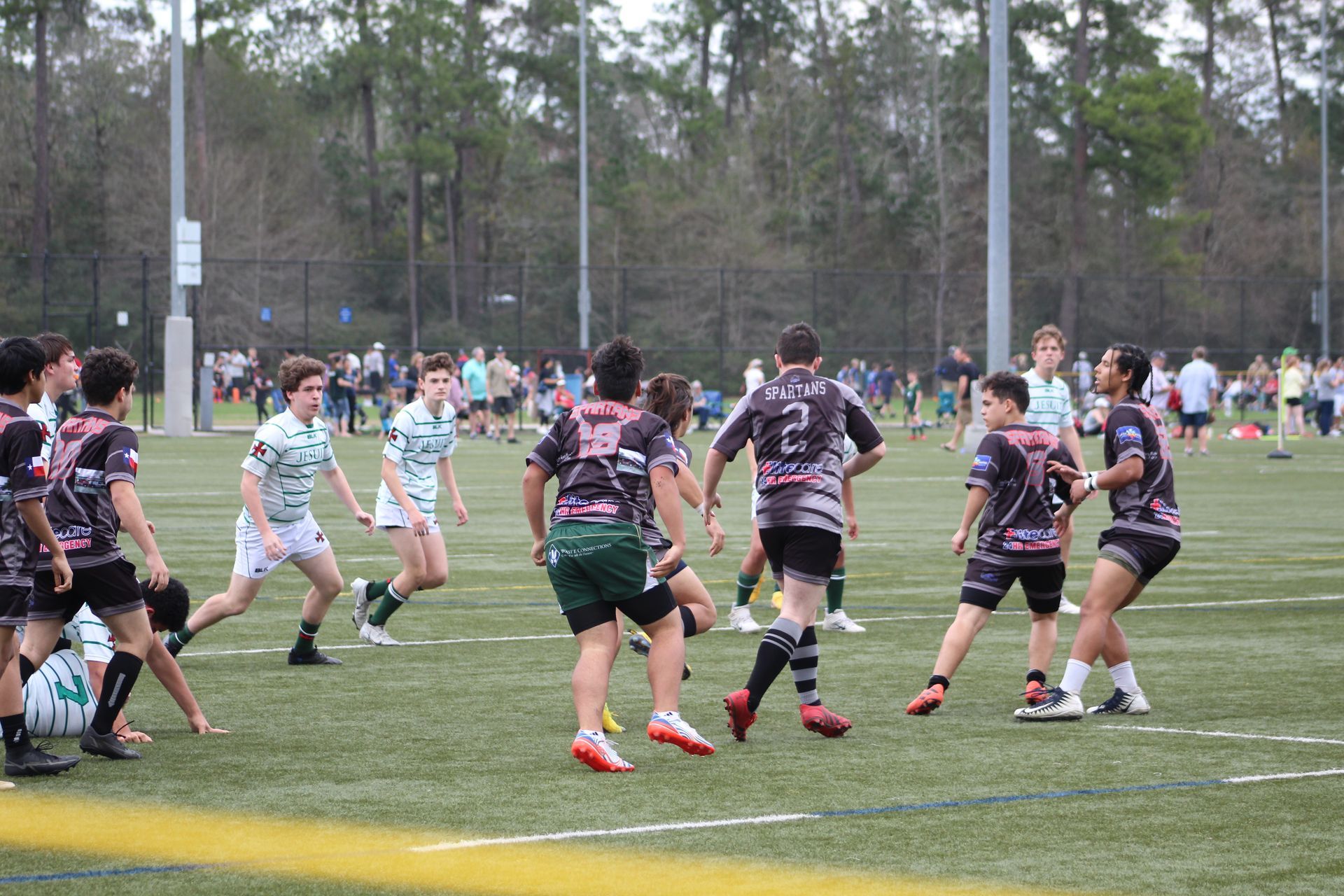 Rugby players on a green field wearing team uniforms. Players running, passing, and competing for the ball.