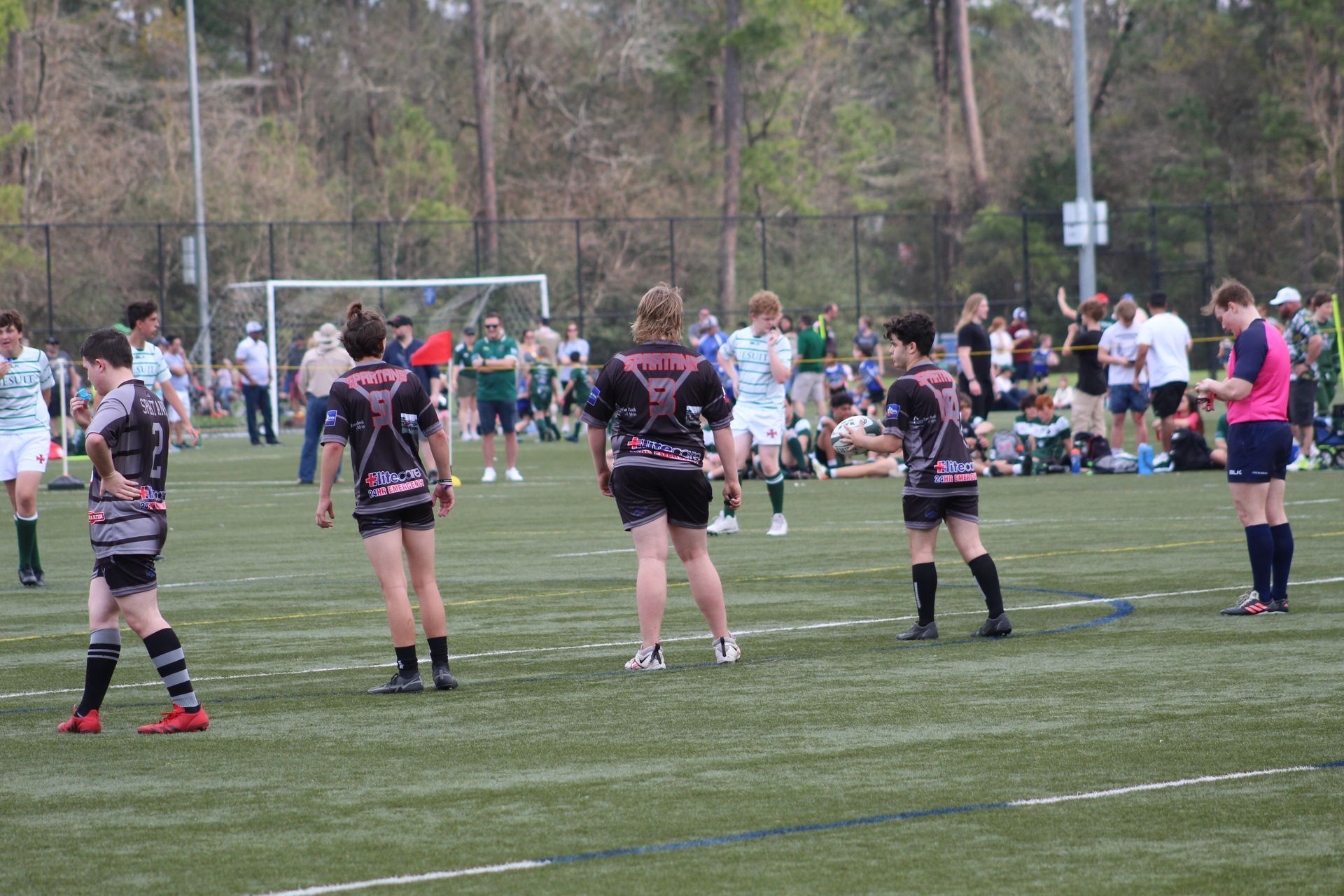 Rugby players in black and pink jerseys on a green field during a game.