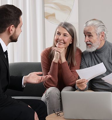 A financial advisor meets with a smiling senior couple, discussing paperwork.