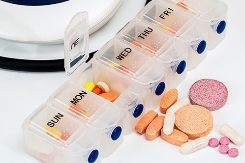 Pill organizer filled with various pills and tablets; a white and blue background.