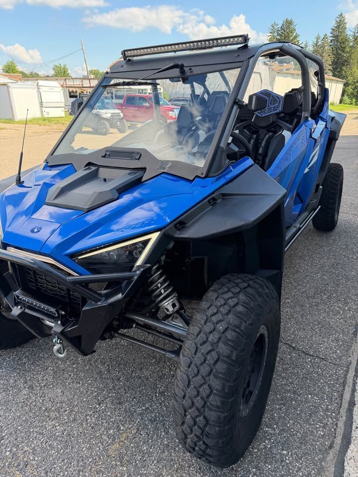 Blue off-road side-by-side ATV parked on pavement, front-left view