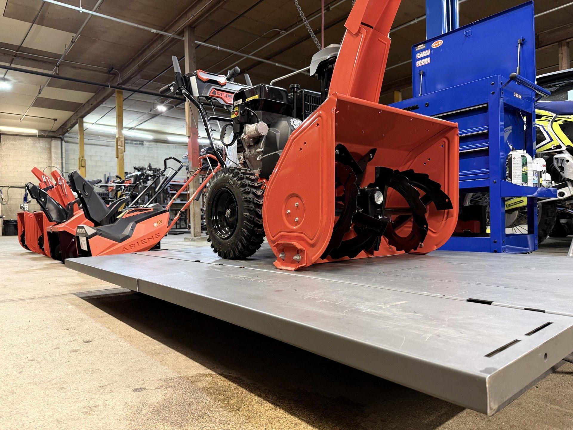 Man in gray uniform operating an Ariens snowblower in a service center.