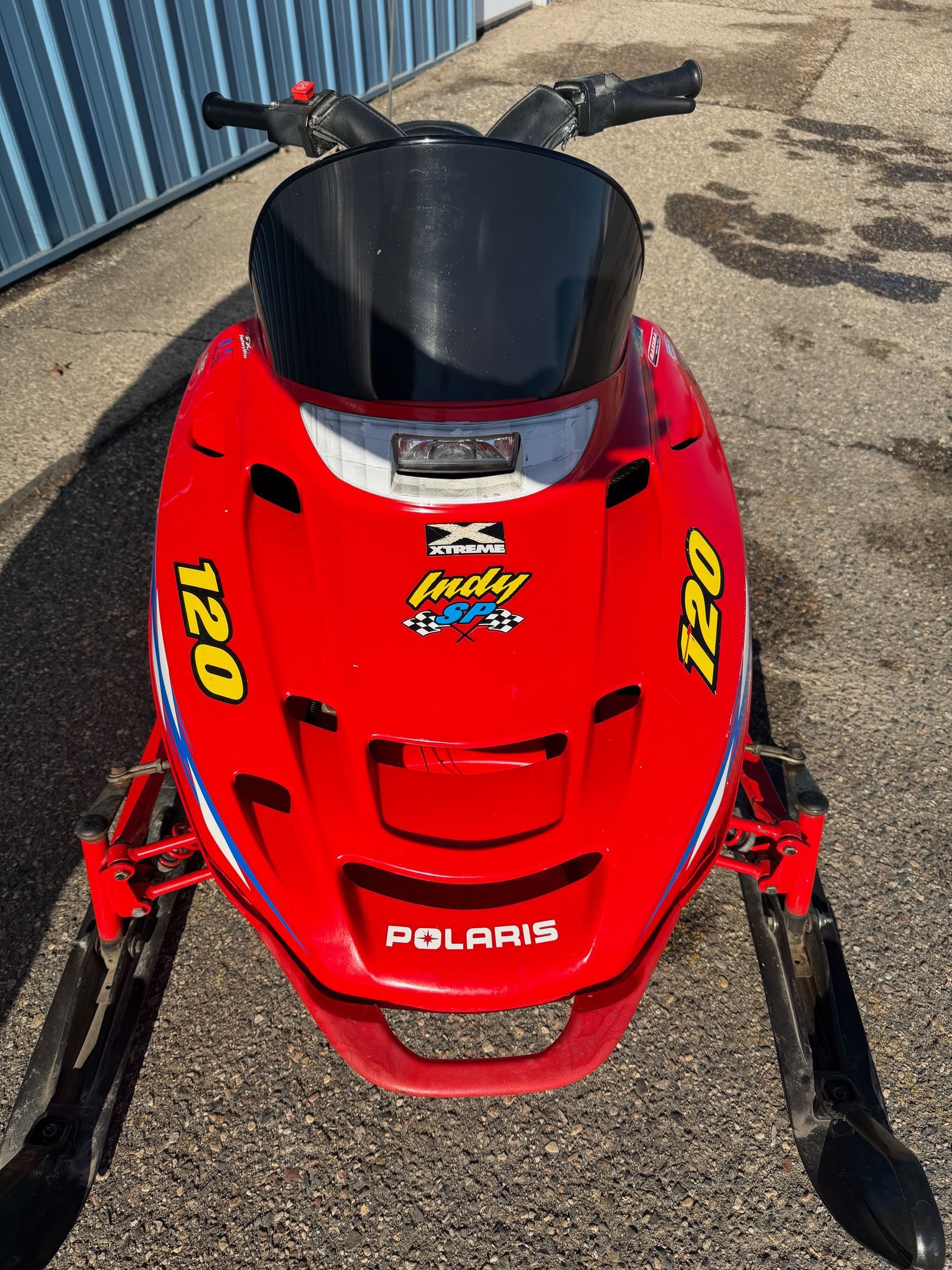 Red Polaris Indy 120 snowmobile, black windshield, two skis, outdoors.